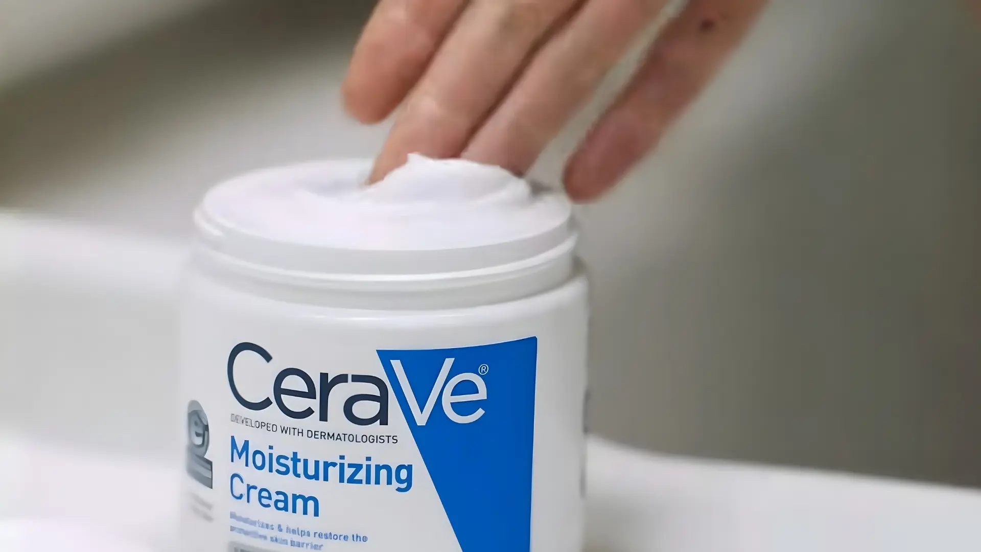 a finger scooping pea sixed amount cream from a cerave jar to demonstrate