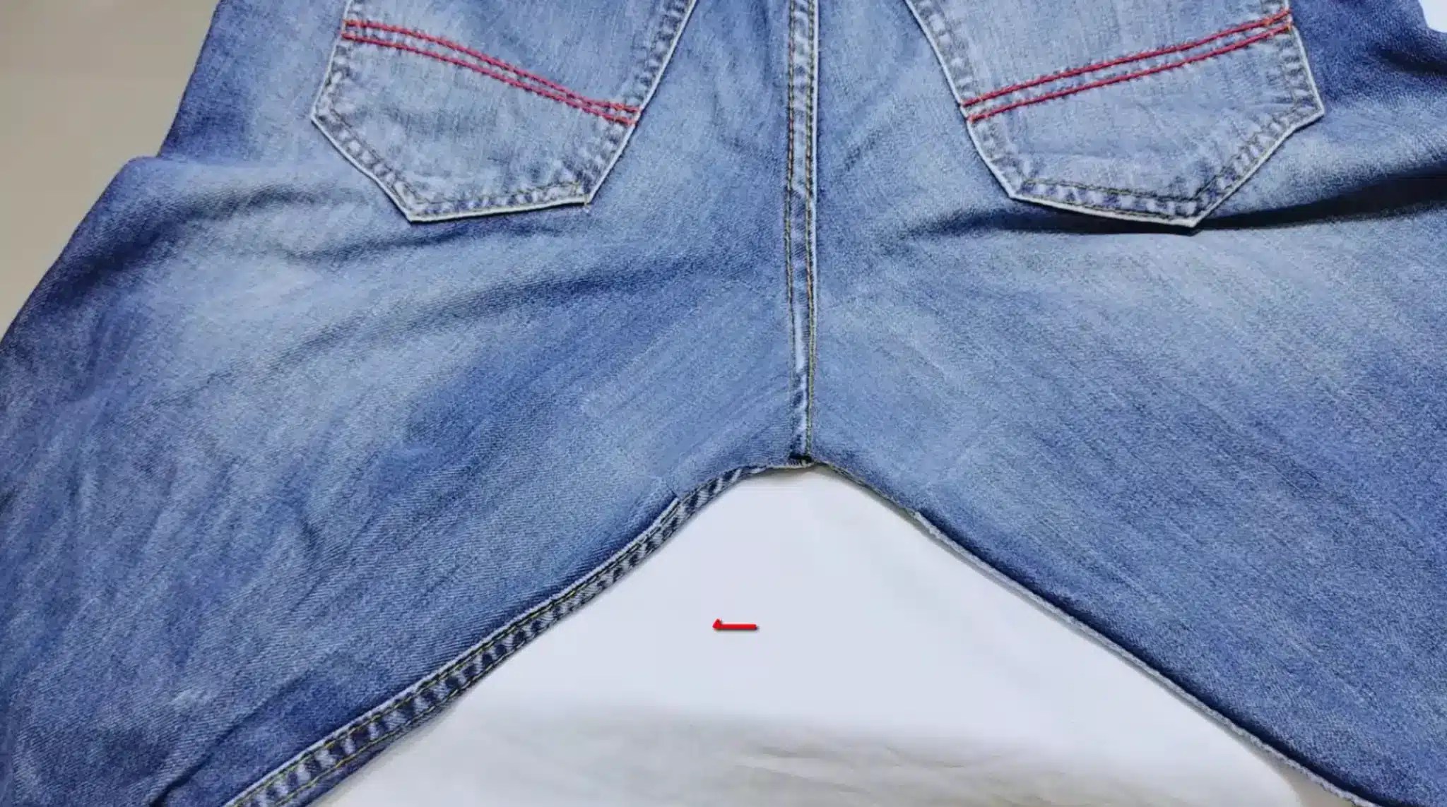 back view of repaired jeans crotch area laid flat, showing smooth denim surface after patching with no visible tears