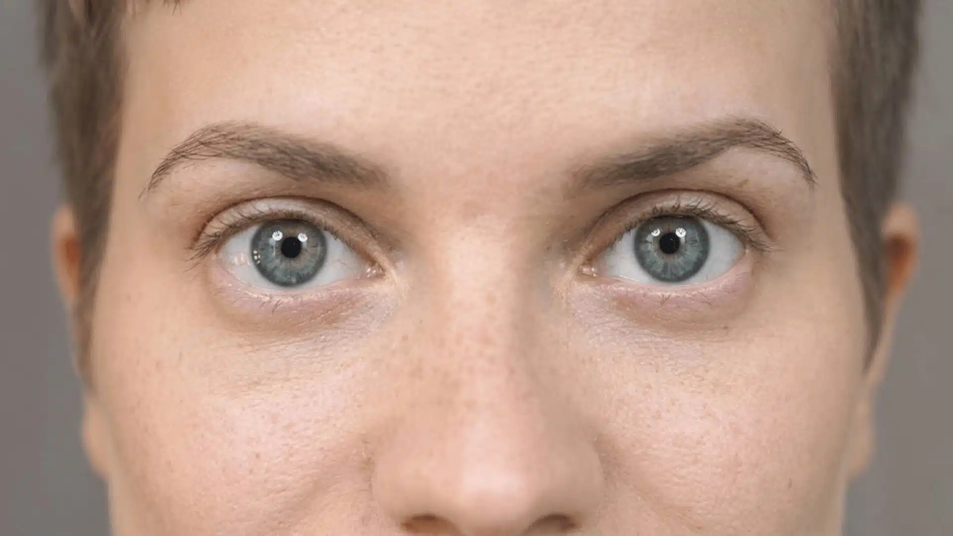 close-up of a caucasian woman's round blue eyes with freckled skin and short hair in 169 ratio.