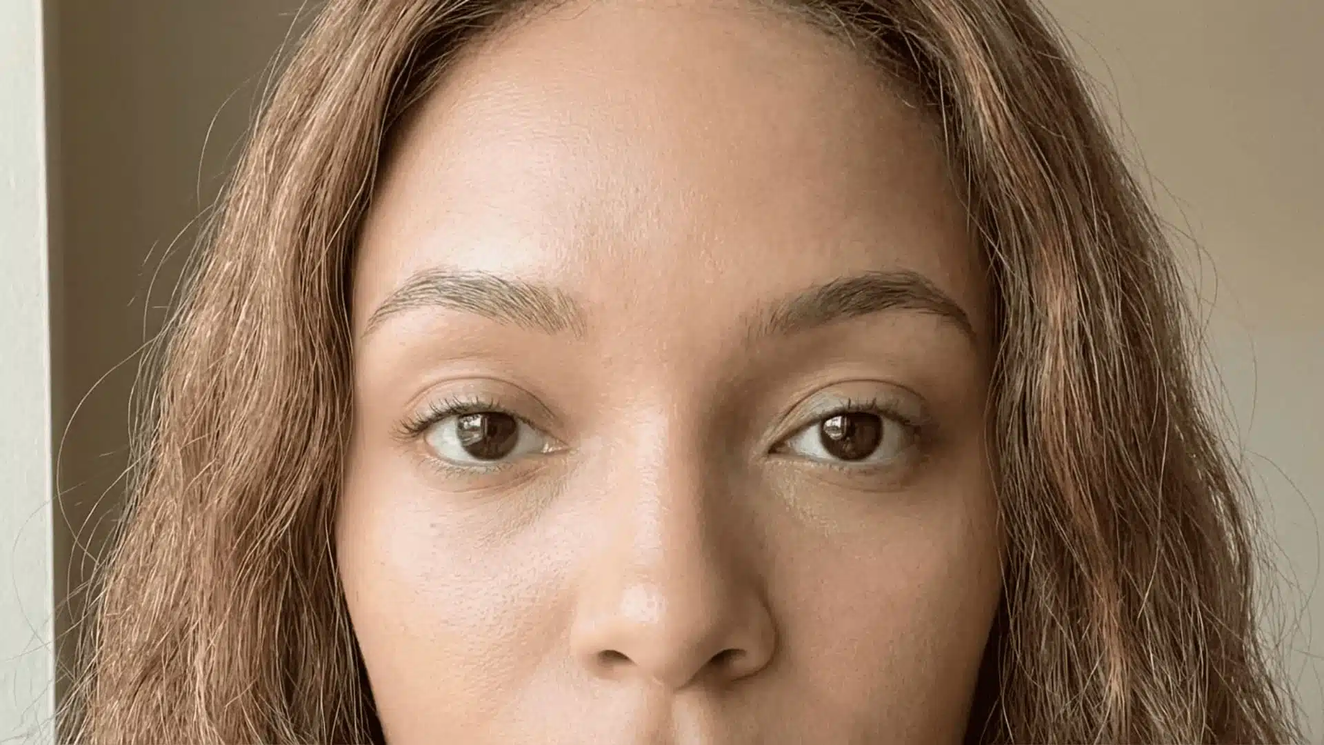 close-up of a woman with warm skin tones, visible natural texture, brown eyes, and realistic stray hair strands