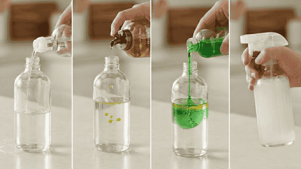 hands adding vinegar, oil, and soap into glass spray bottle, then shaking homemade cleaner mixture on kitchen counter.webp