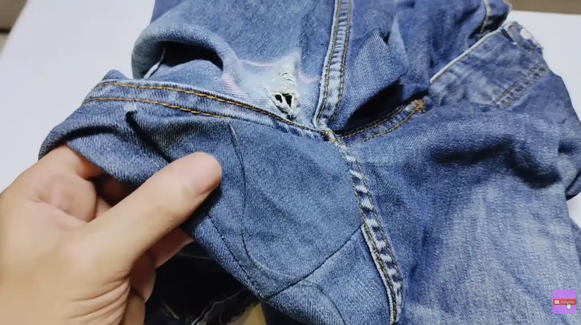 hands showing inner denim patch placed behind torn jeans crotch area, preparing fabric for stitching repair