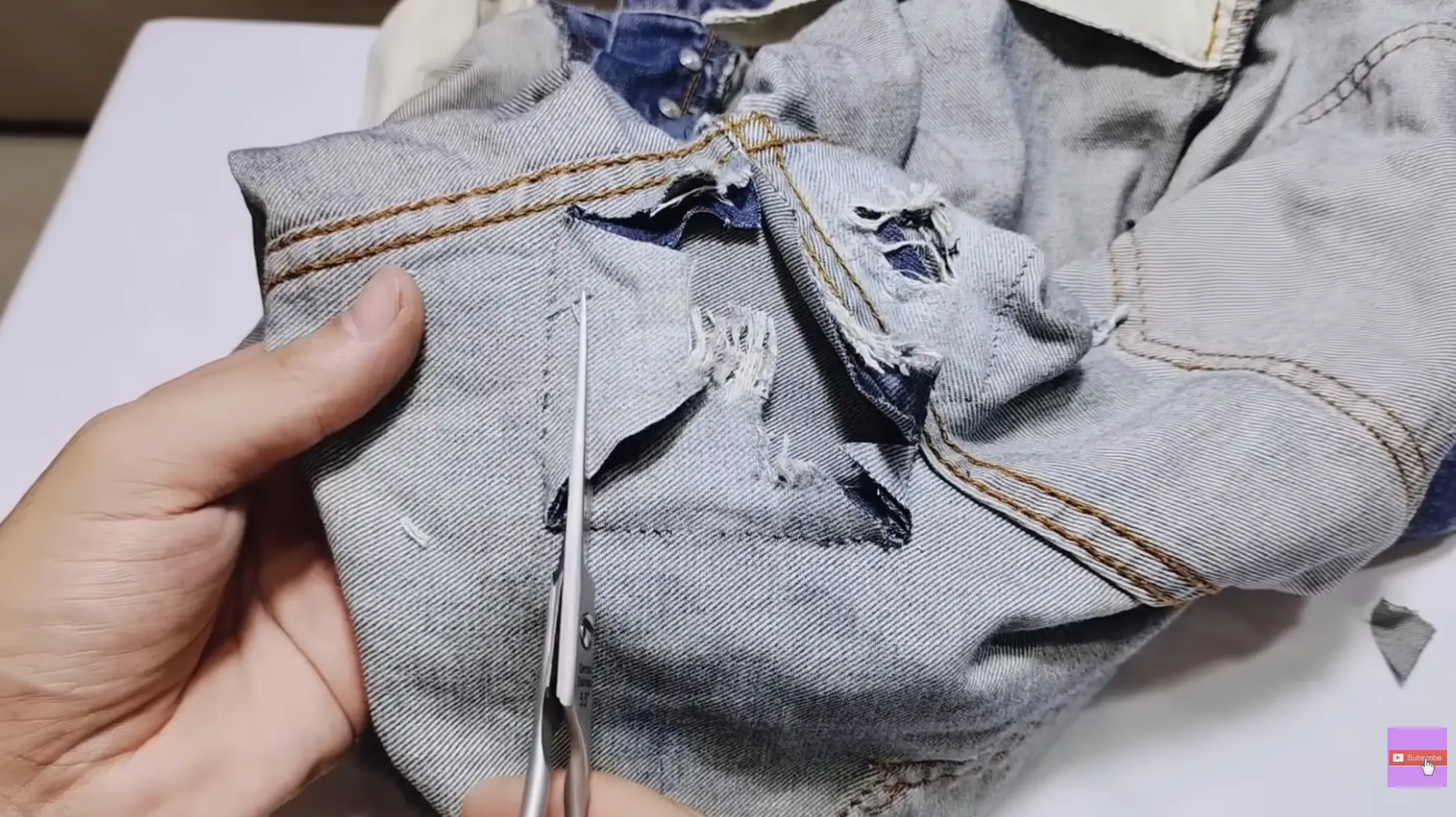hands trimming frayed threads from torn jeans crotch area with scissors, preparing damaged denim fabric for patching