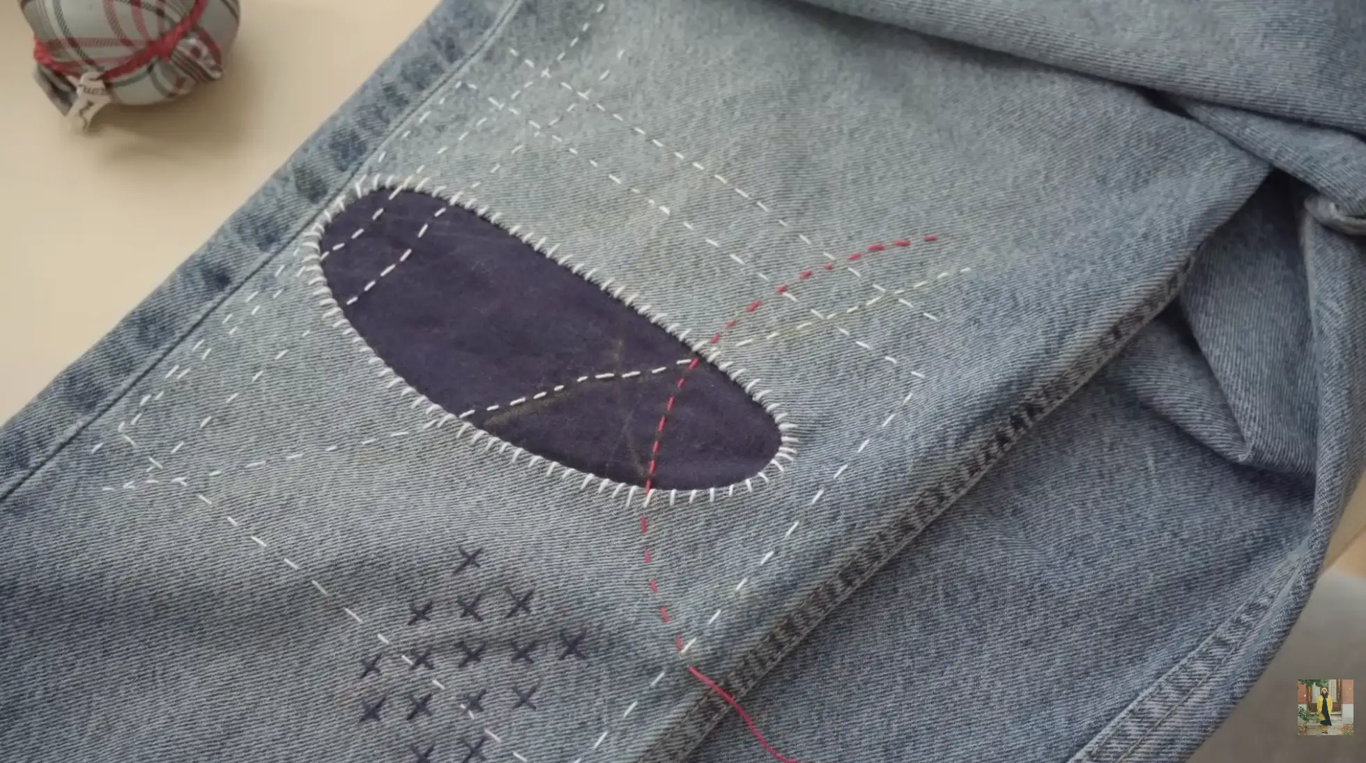 jeans repaired with sashiko stitching and inner denim patch, showing decorative cross stitches and lines around hole