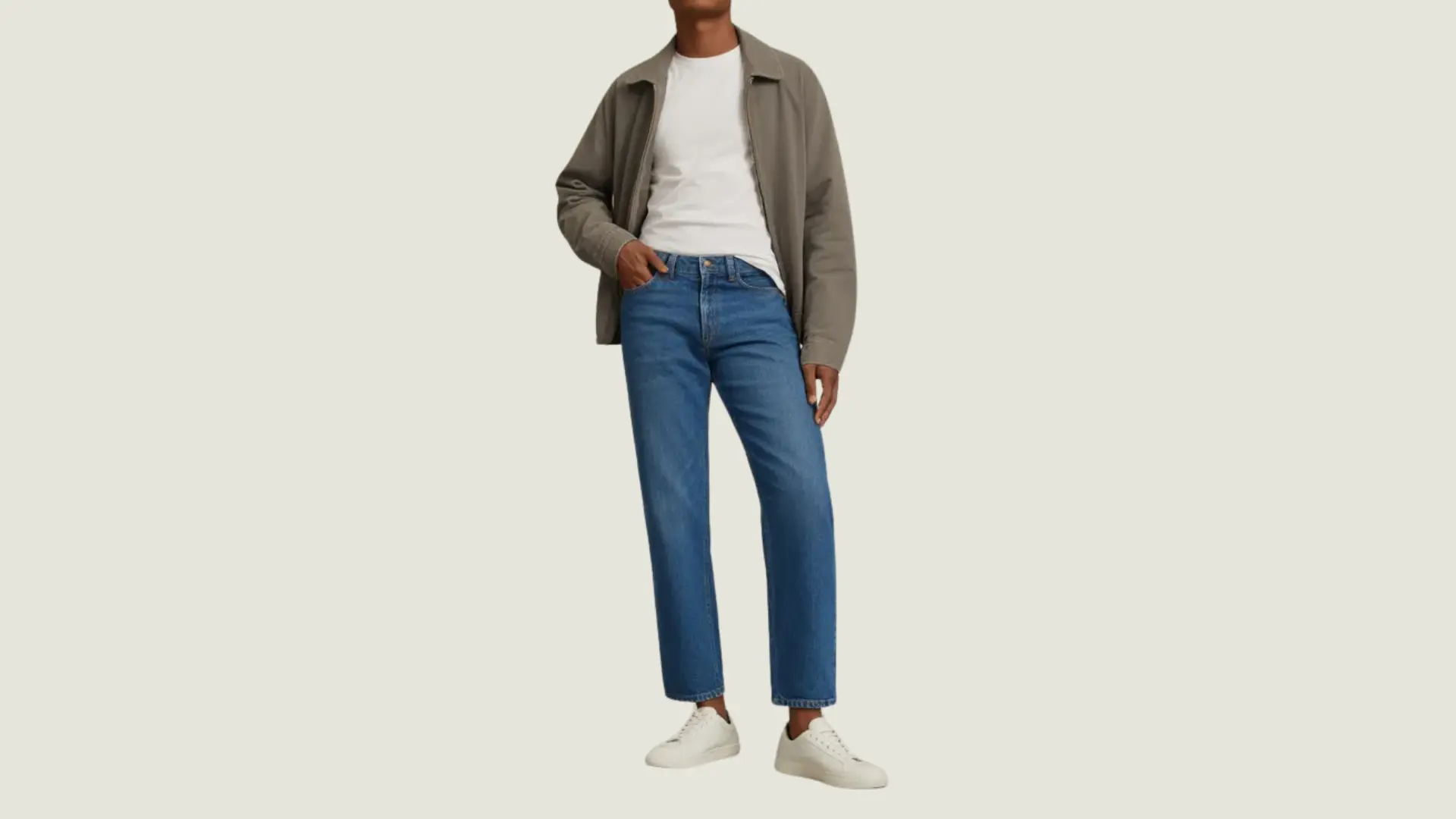 man in a normcore style wearing a grey zip-up jacket, white t-shirt, blue jeans, and white sneakers
