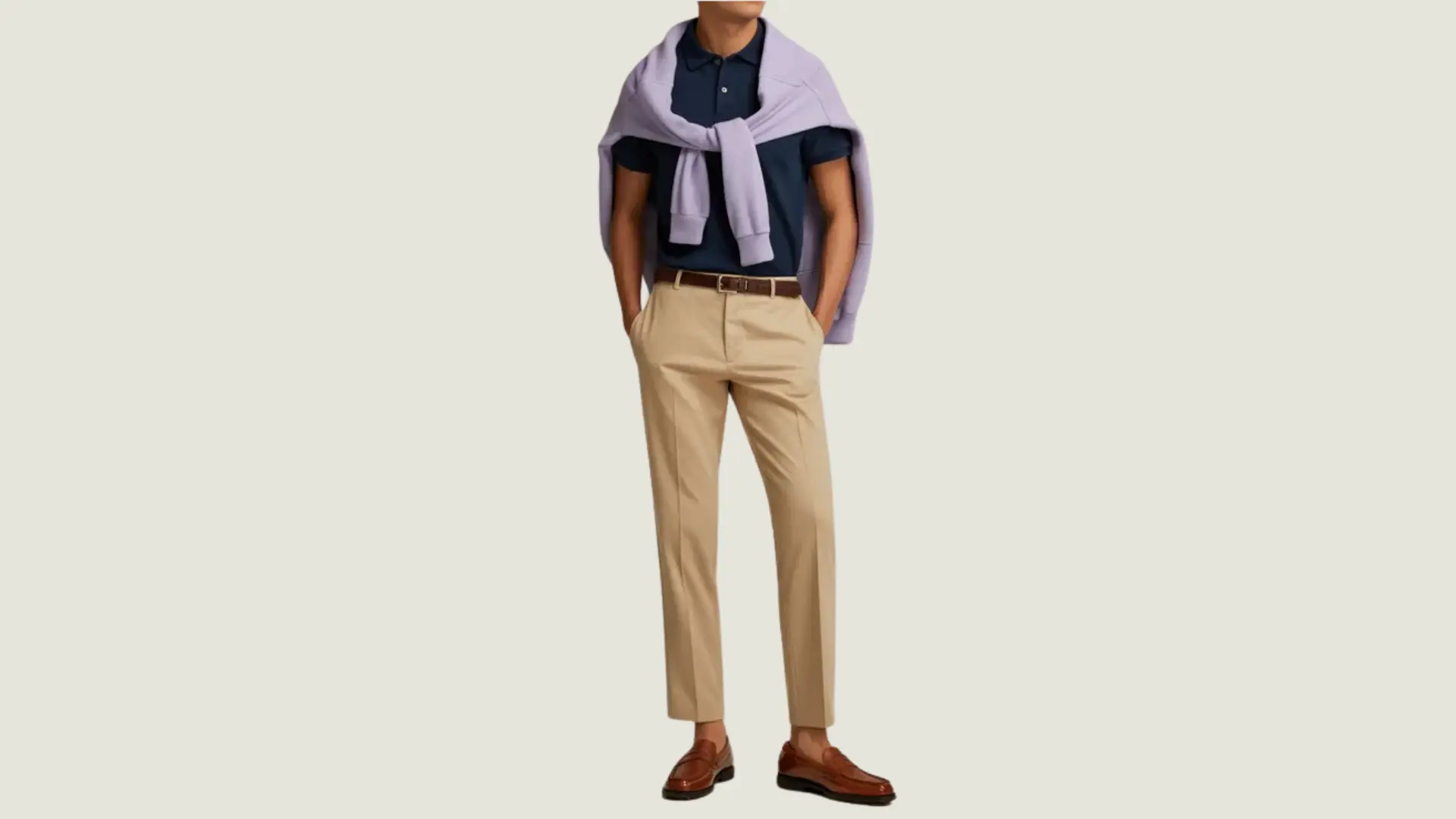 man in a preppy style wearing a navy polo, lilac sweater over shoulders, and tan chinos with loafers