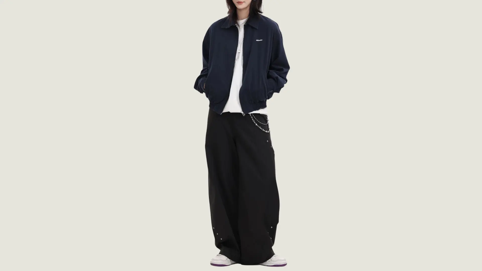 person in androgynous style wearing a navy bomber jacket over a white tee with black wide-leg trousers and sneakers