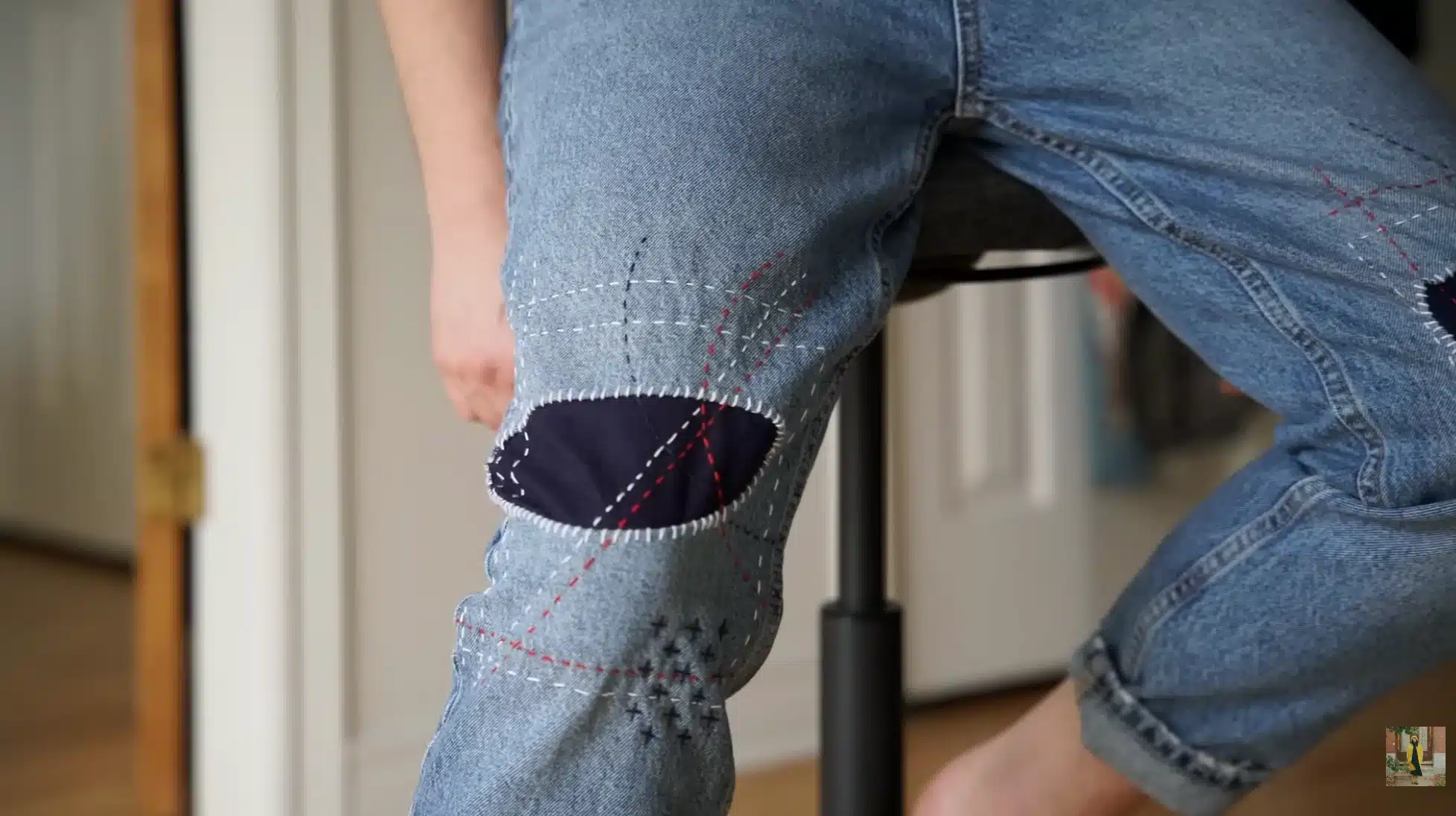 person wearing repaired jeans with visible sashiko stitched knee patch, showing decorative stitches and denim repair