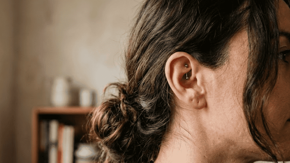 side profile of ear with a rook piercing on upper inner cartilage, hair in low bun, warm indoor light