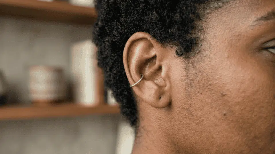 side profile of ear with a silver outer conch hoop, short curly hair, soft indoor light and blurred shelf background