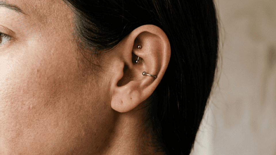 side profile of ear with a snug piercing bar through inner cartilage, soft indoor light and neutral background