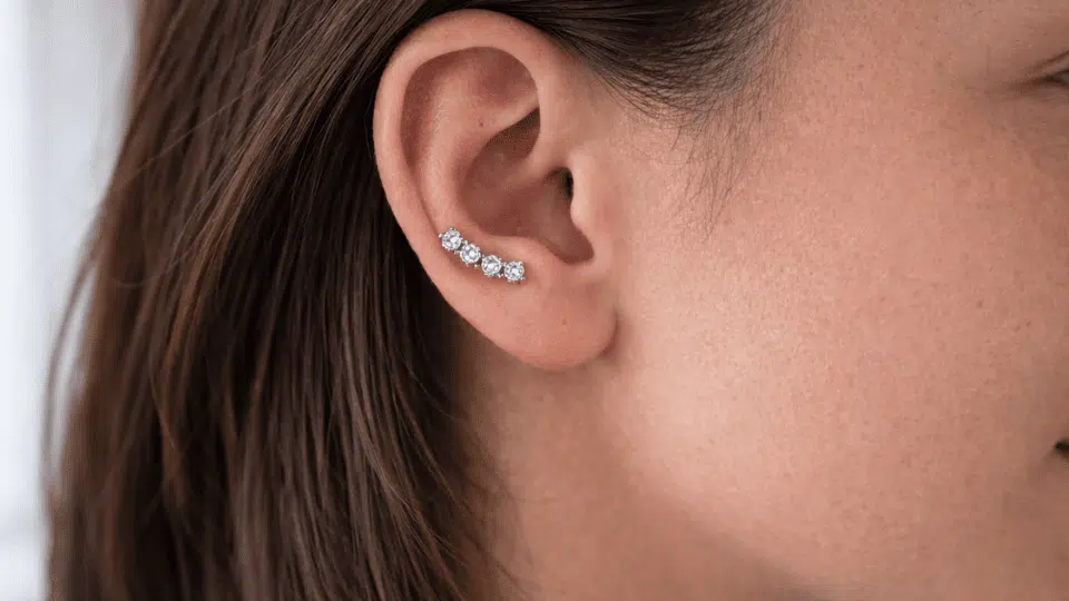 side profile of ear with small curved auricle stud, brown hair tucked back, soft indoor daylight background