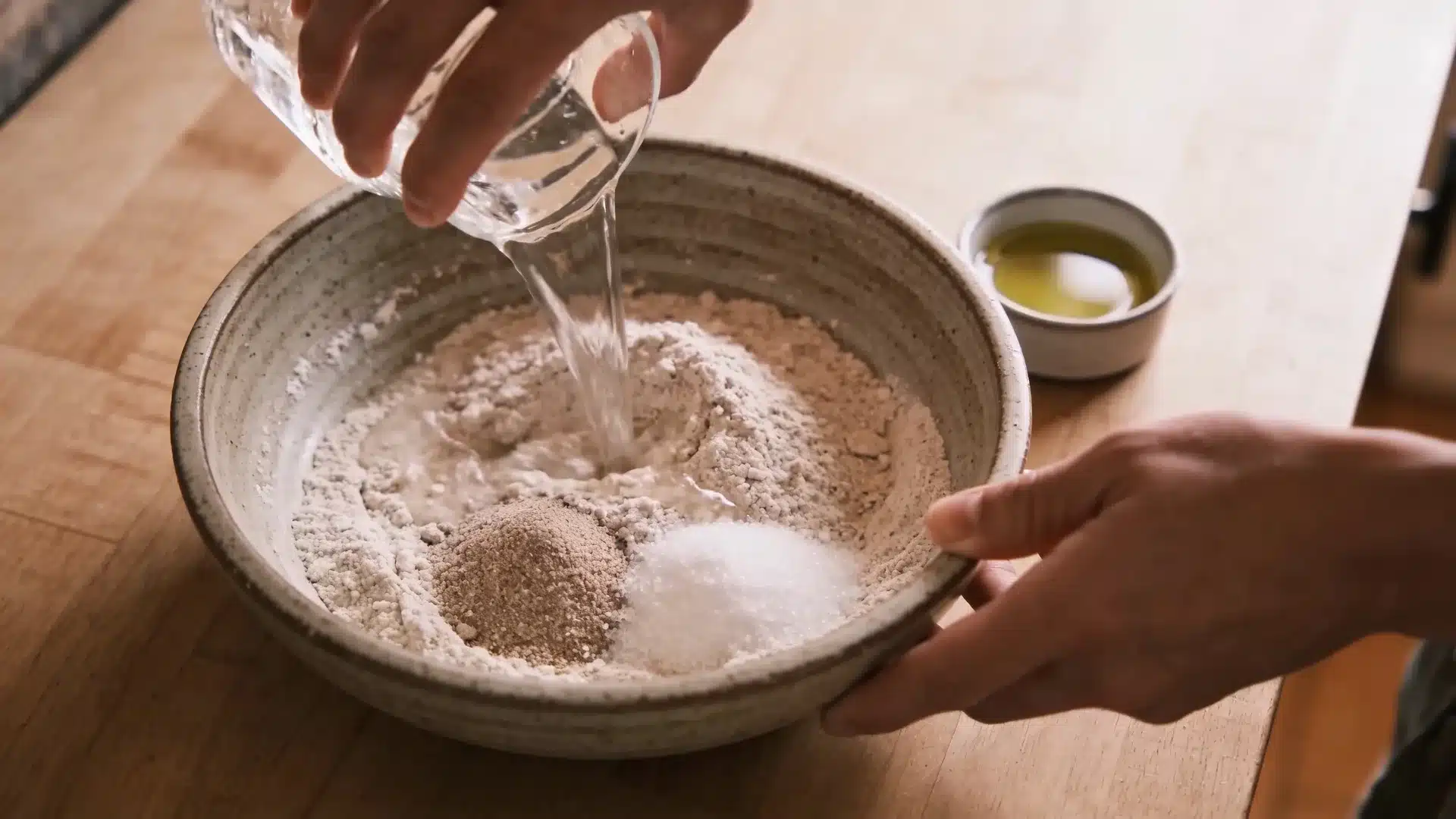 the image shows a person pouring water into a bowl of flour, yeast, and salt for making flatbread dough