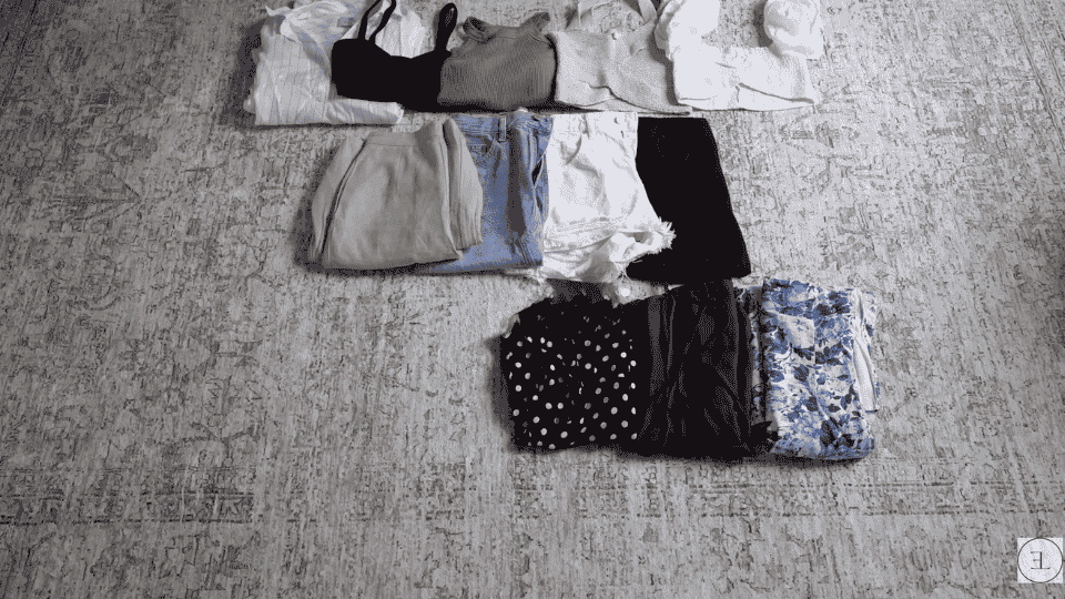 travel clothes arranged in groups on the floor to prepare for how to pack a suitcase efficiently