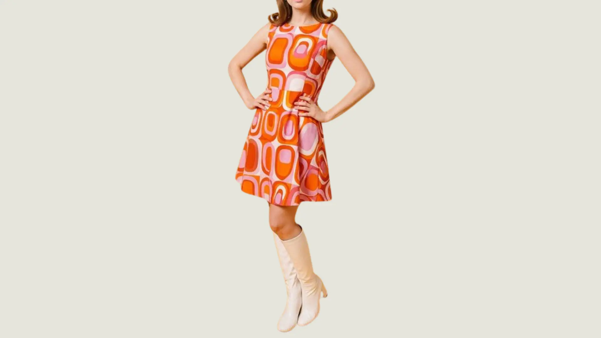 woman in a 70s disco style wearing a sleeveless orange and pink geometric mini dress with tall white go-go boots