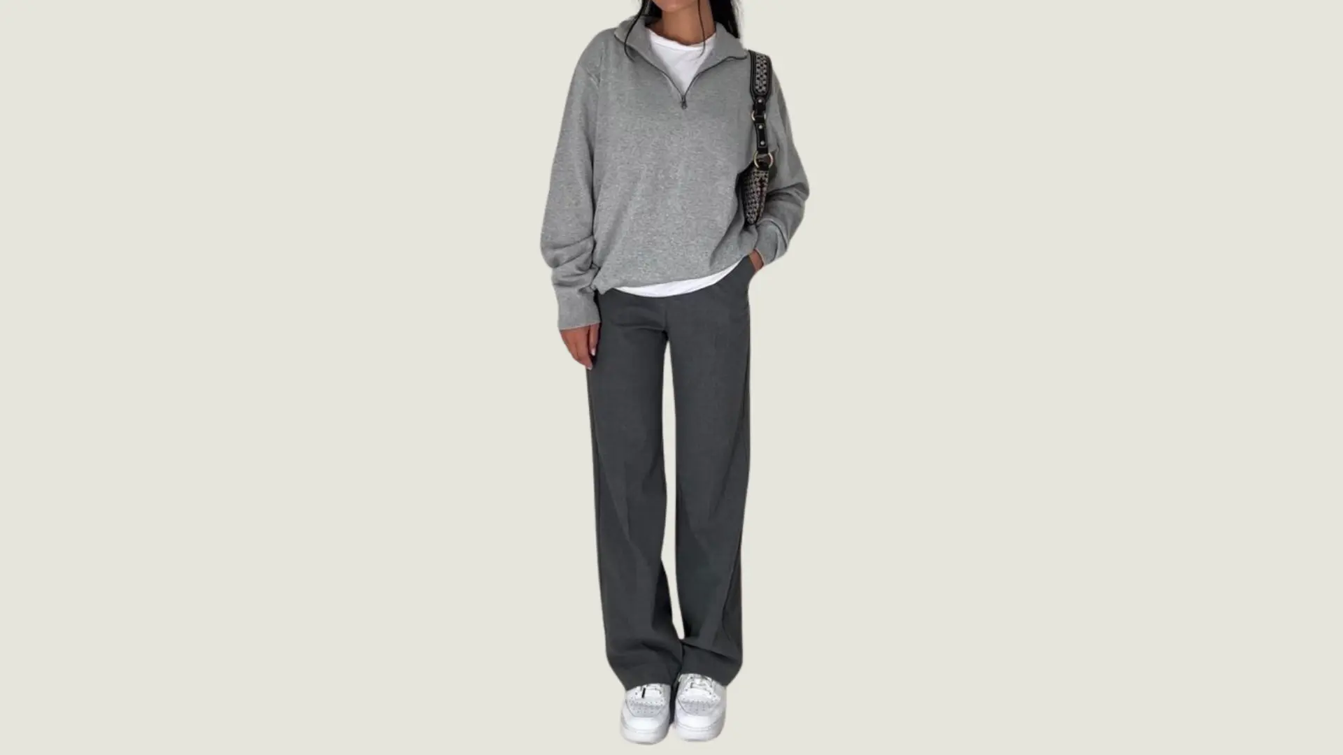 woman in a casual style wearing a grey quarter-zip sweatshirt, charcoal trousers, and white sneakers