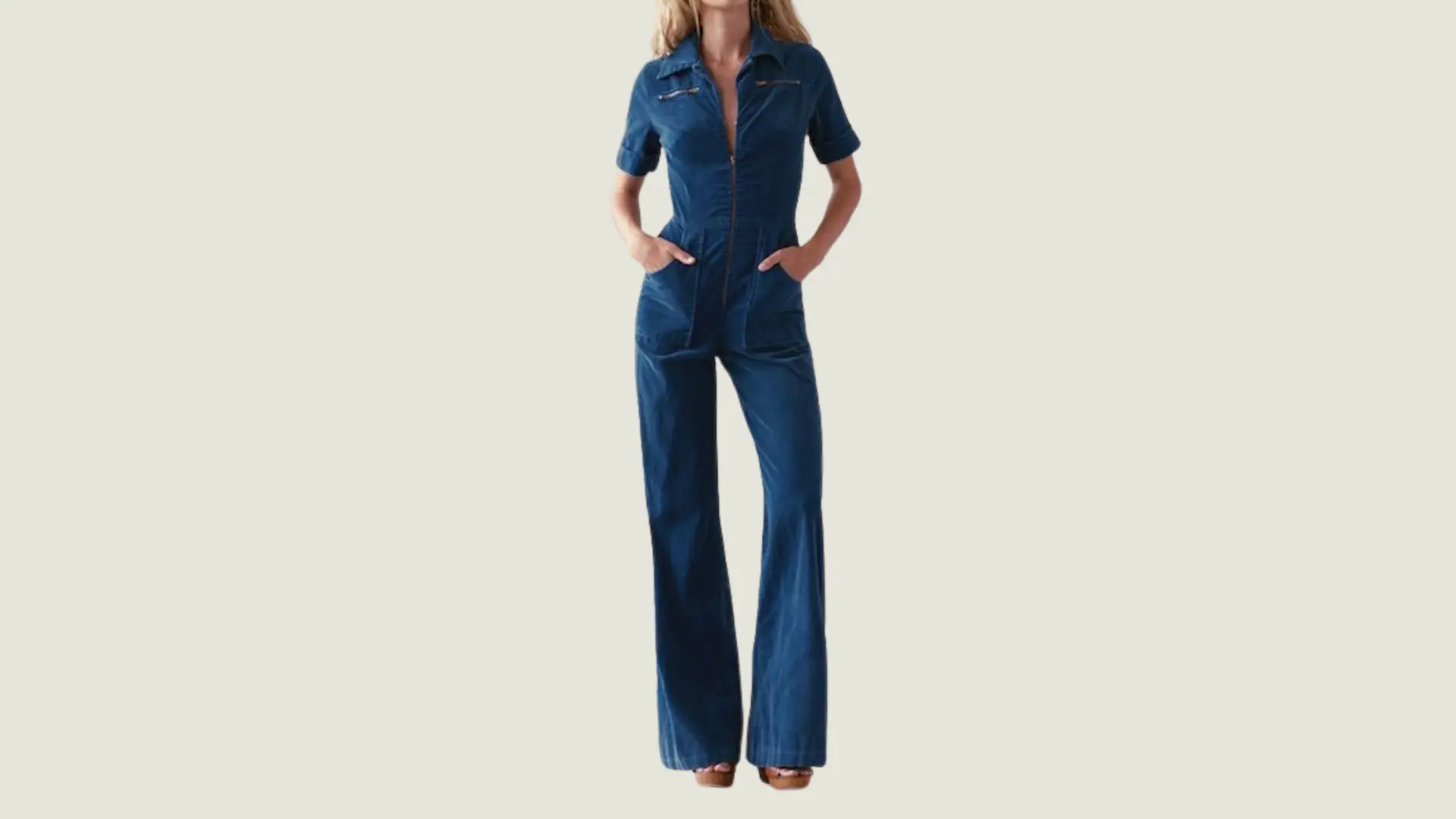 woman in a retro style wearing a short-sleeved blue denim jumpsuit with flared legs and platform wooden sandals