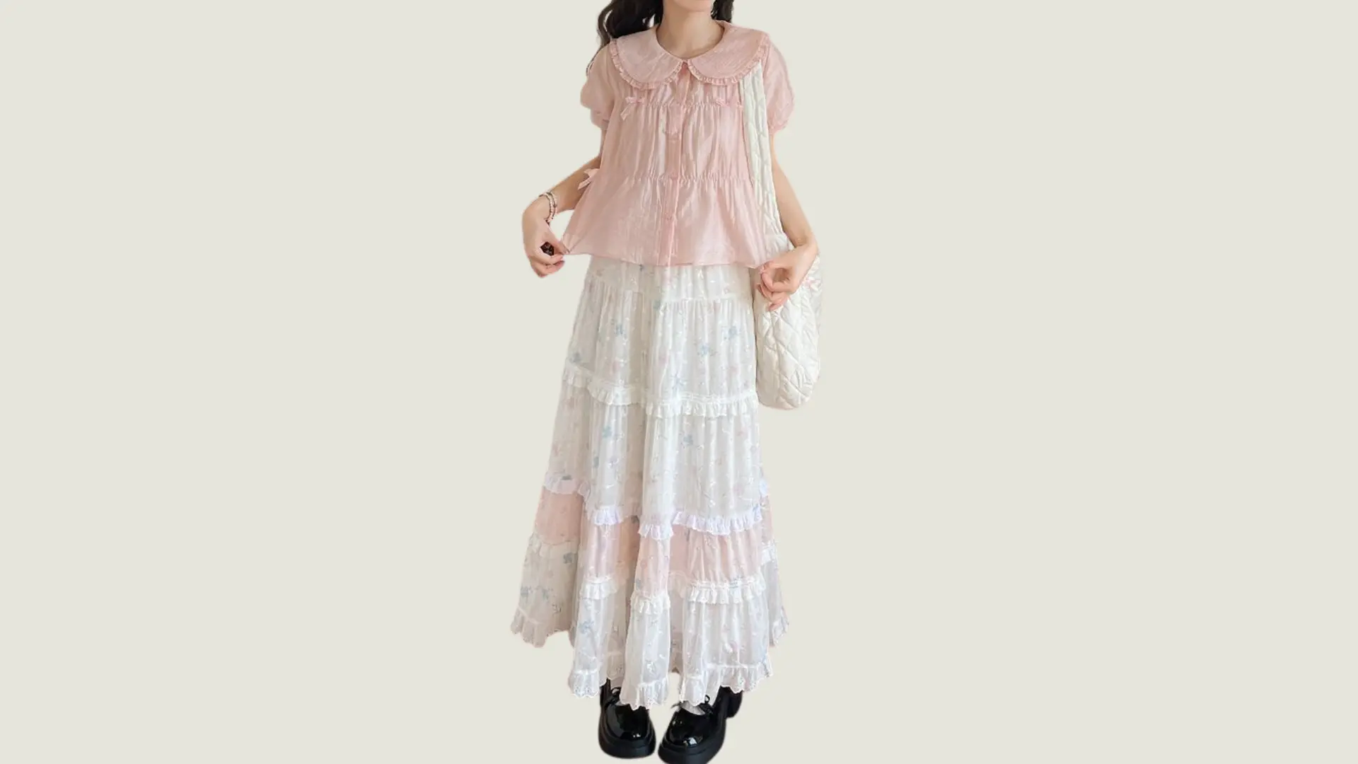 woman in cottagecore style wearing a pink ruffled blouse and a tiered floral maxi skirt with a white quilted bag