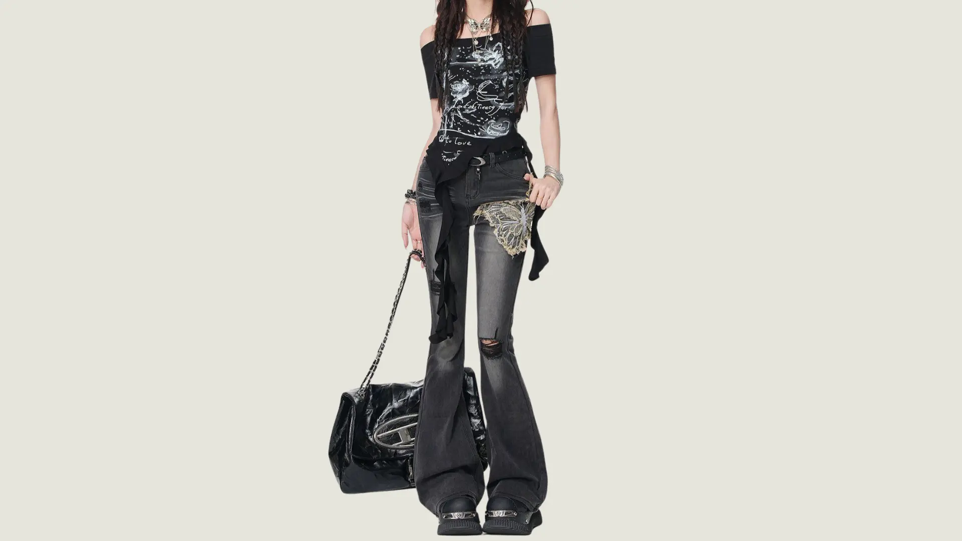 woman in edgy_grunge style wearing an off-shoulder graphic top and ripped flared jeans with a large black leather bag