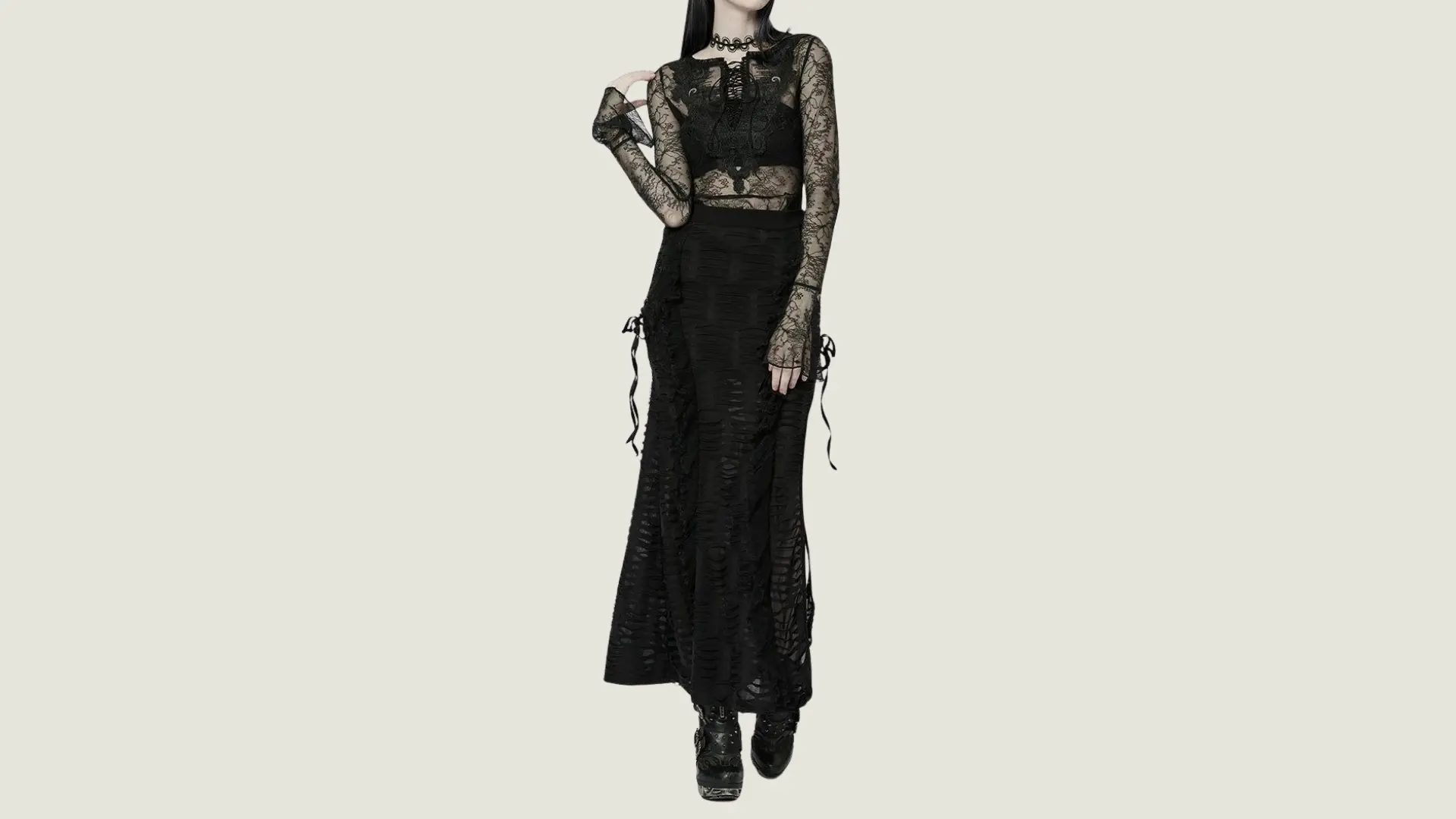 woman in gothic style wearing a black lace long-sleeved top over a bralette with a shredded black maxi skirt and boots