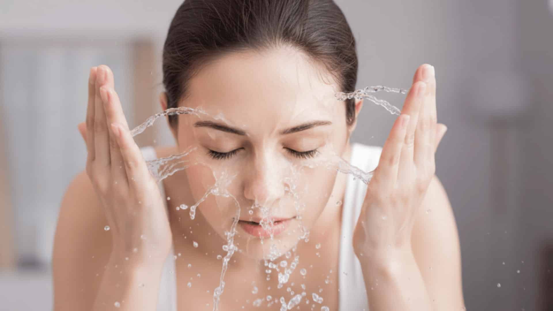 woman splashing water on her face while washing skin in bathroom sink close up with eyes closed and droplets midair