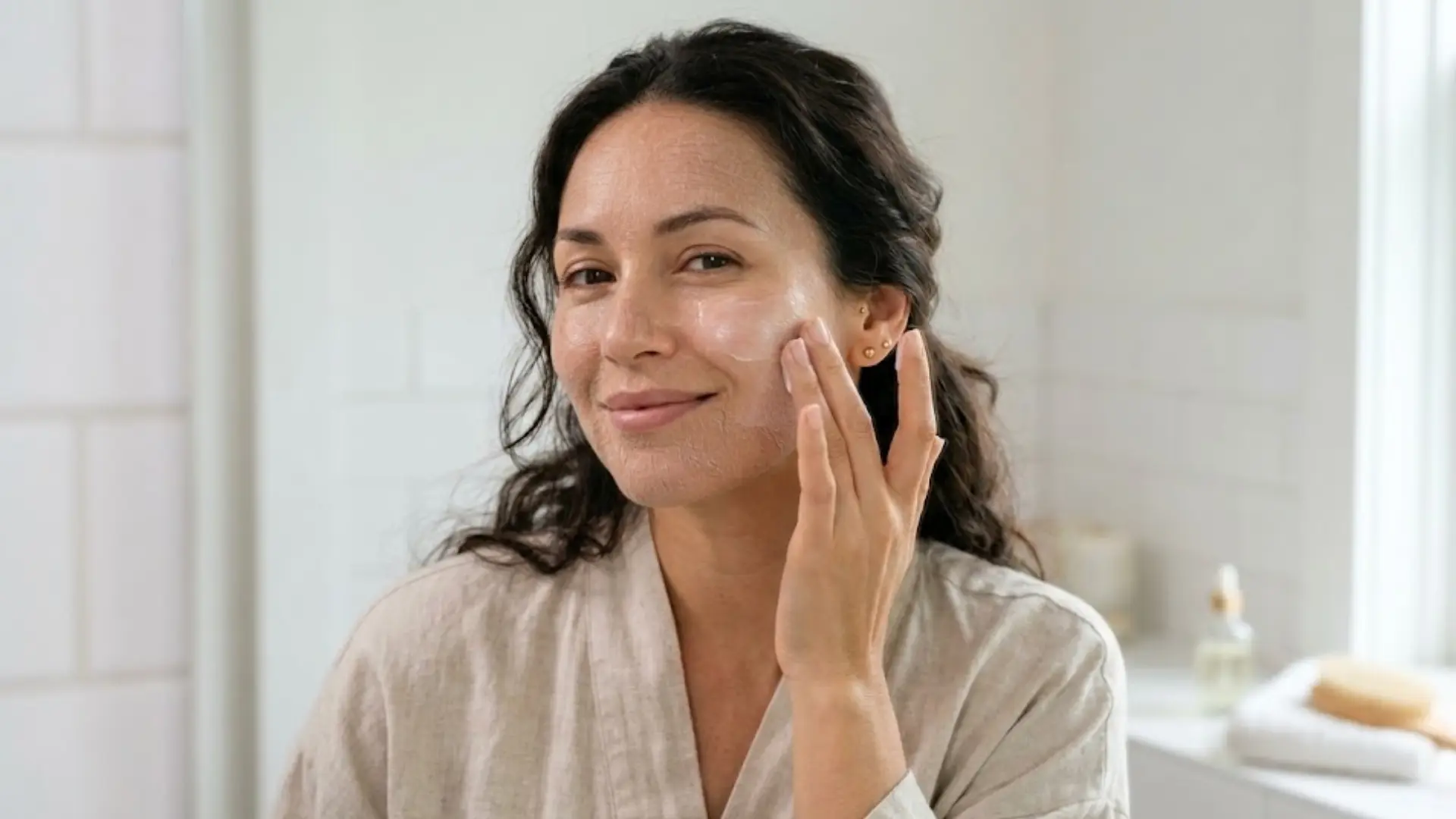 woman with dry skin applying cerave moisturizer to her cheek in a bright white bathroom