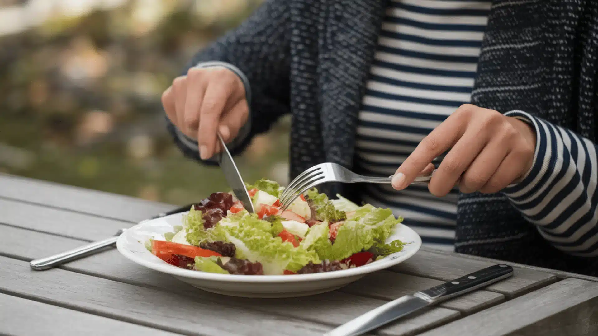 women holding a knife and a fork, poised to cut and eat a fresh salad placed on a white plate