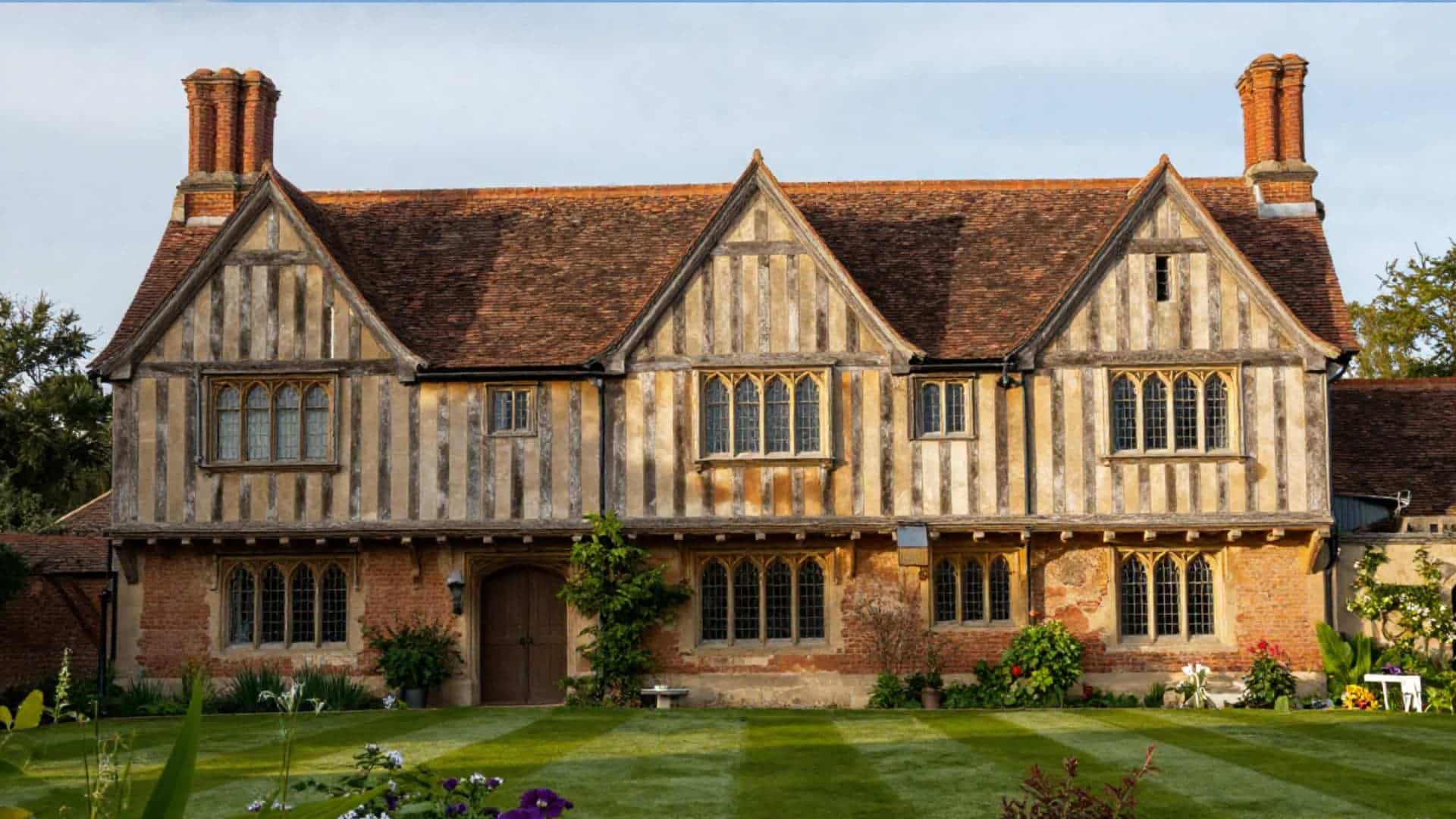 traditional tudor-style house with steep gabled roof, decorative half-timber framing, tall brick chimneys, narrow multi-pane windows