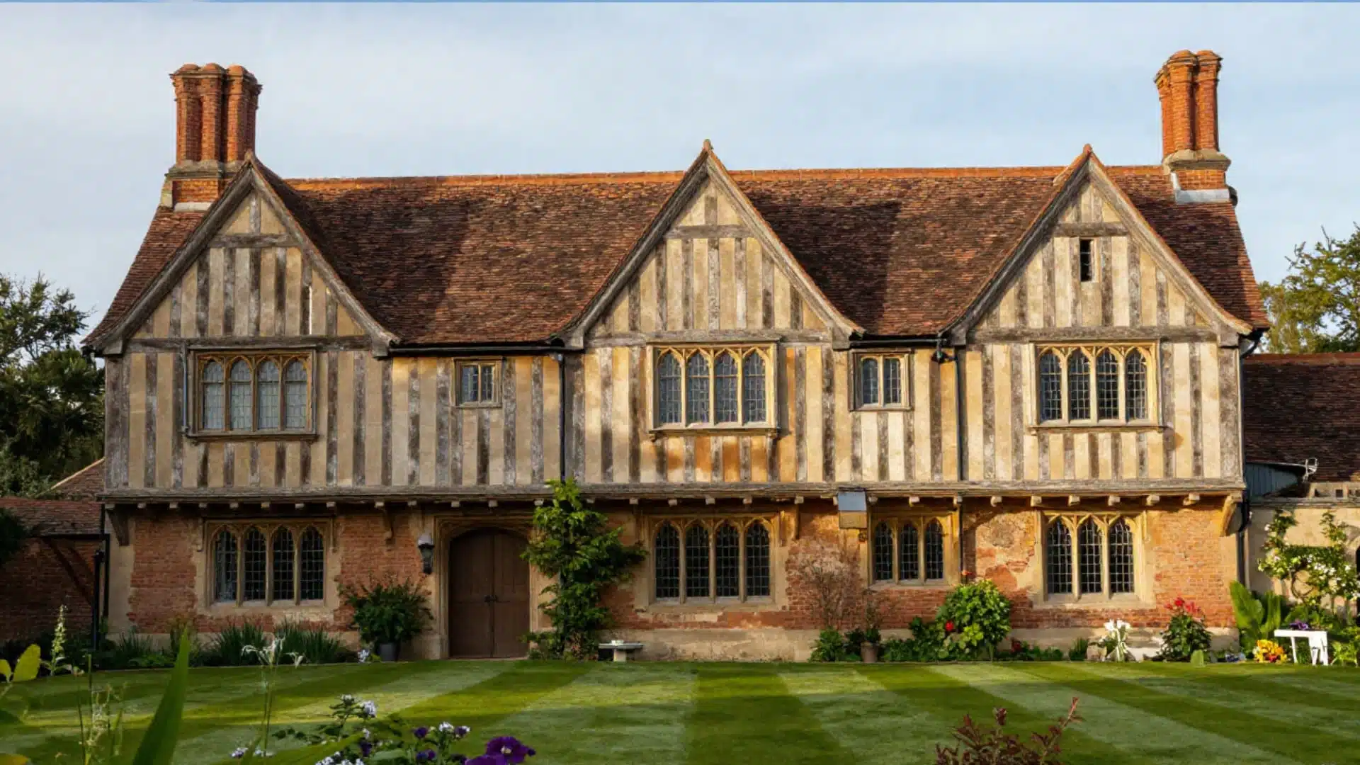 traditional tudor-style house with steep gabled roof, decorative half-timber framing, tall brick chimneys, narrow multi-pane windows