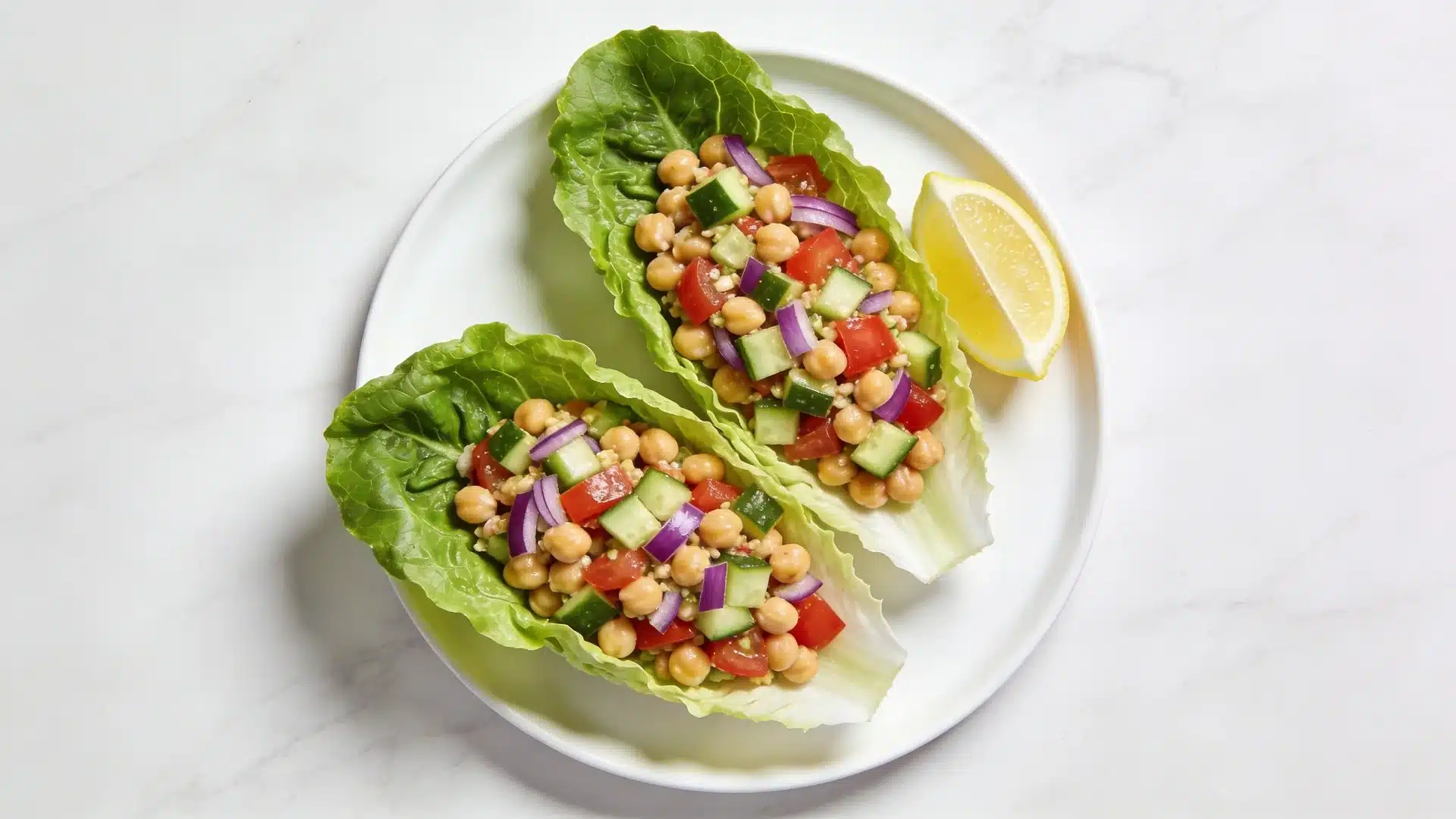 two romaine lettuce cups filled with chickpea salad, cucumber, tomato, and red onion, served on plate with lemon wedge