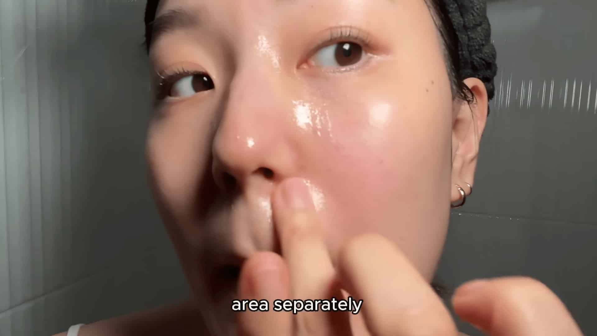 young woman applying skincare product to nose area separately in bathroom close up with wet glowing skin