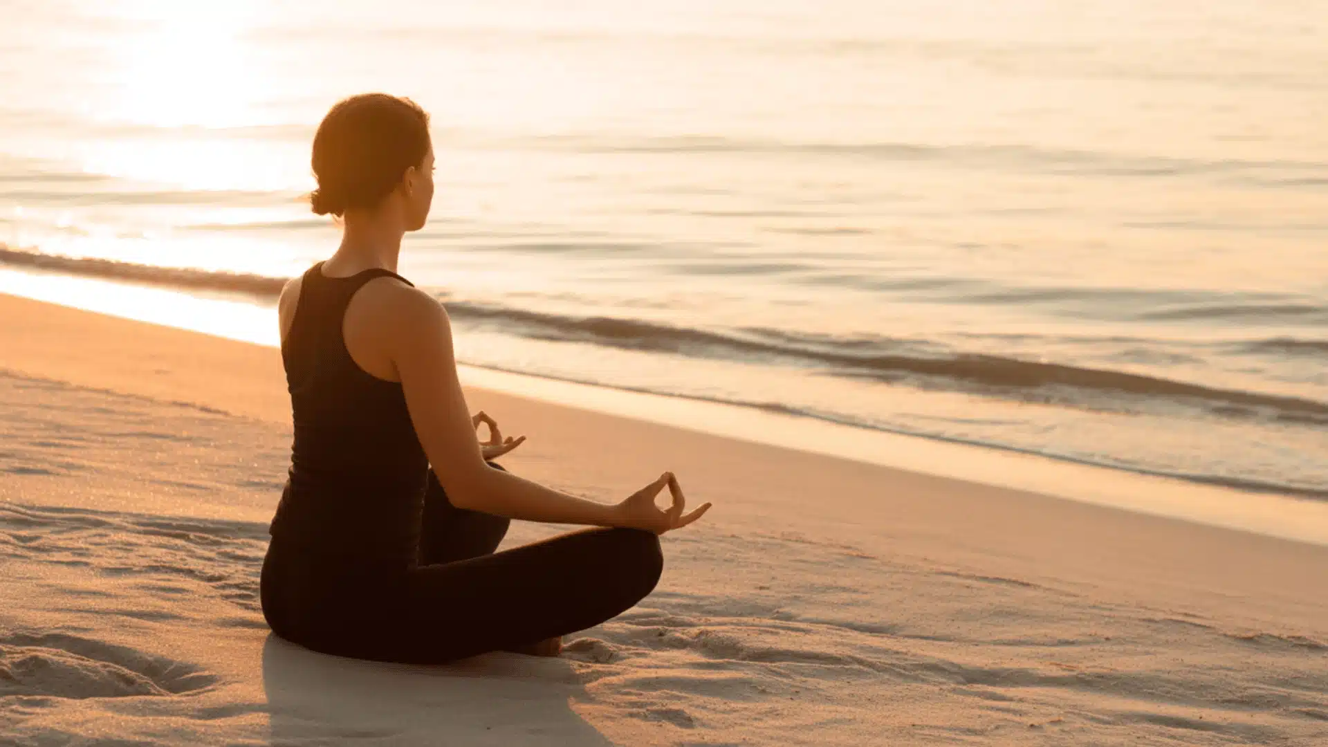 serene photograph of a person meditating in a lotus position on a sandy beach at sunset