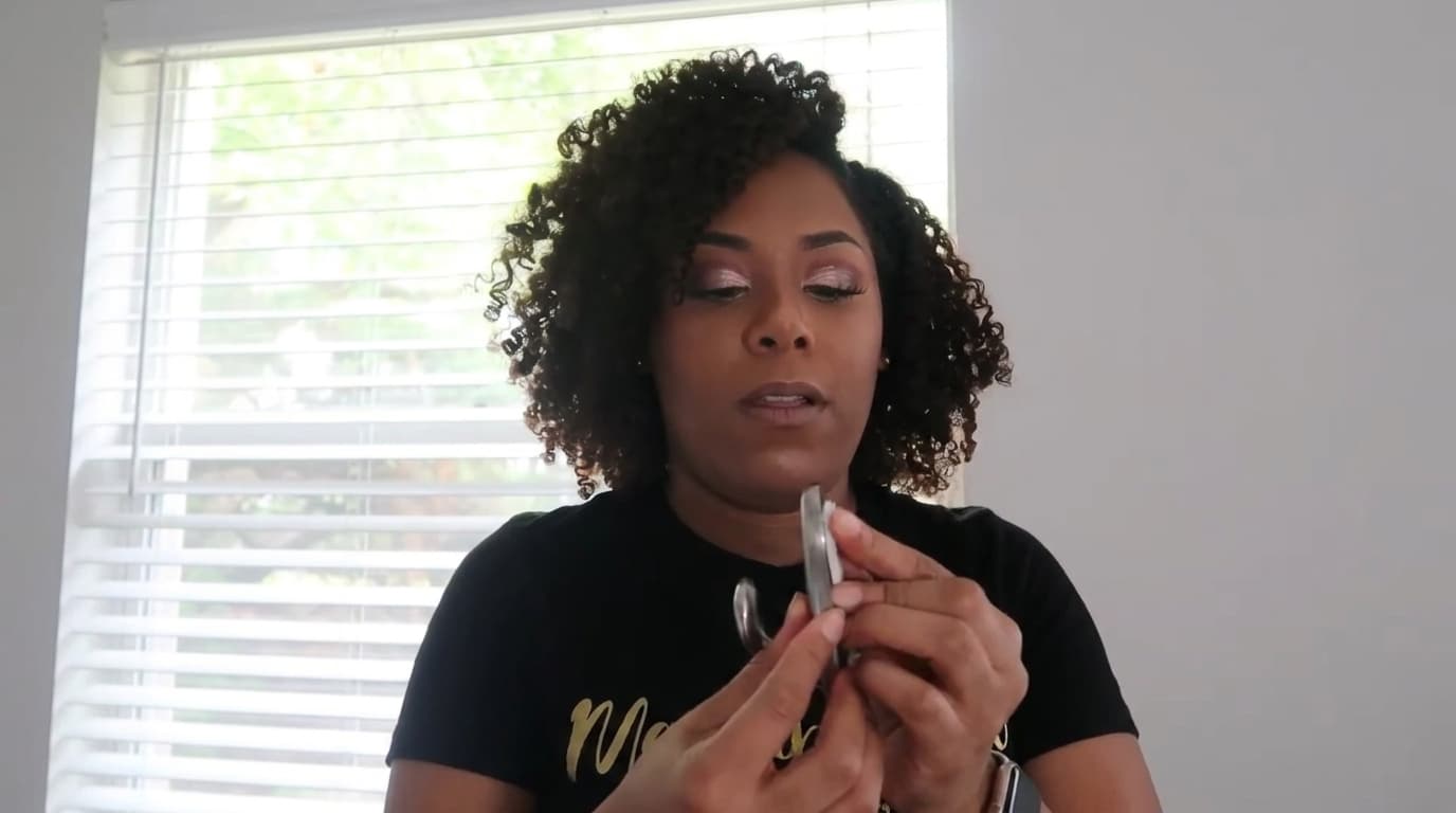 woman holding metal command hook in front of window blinds inside home