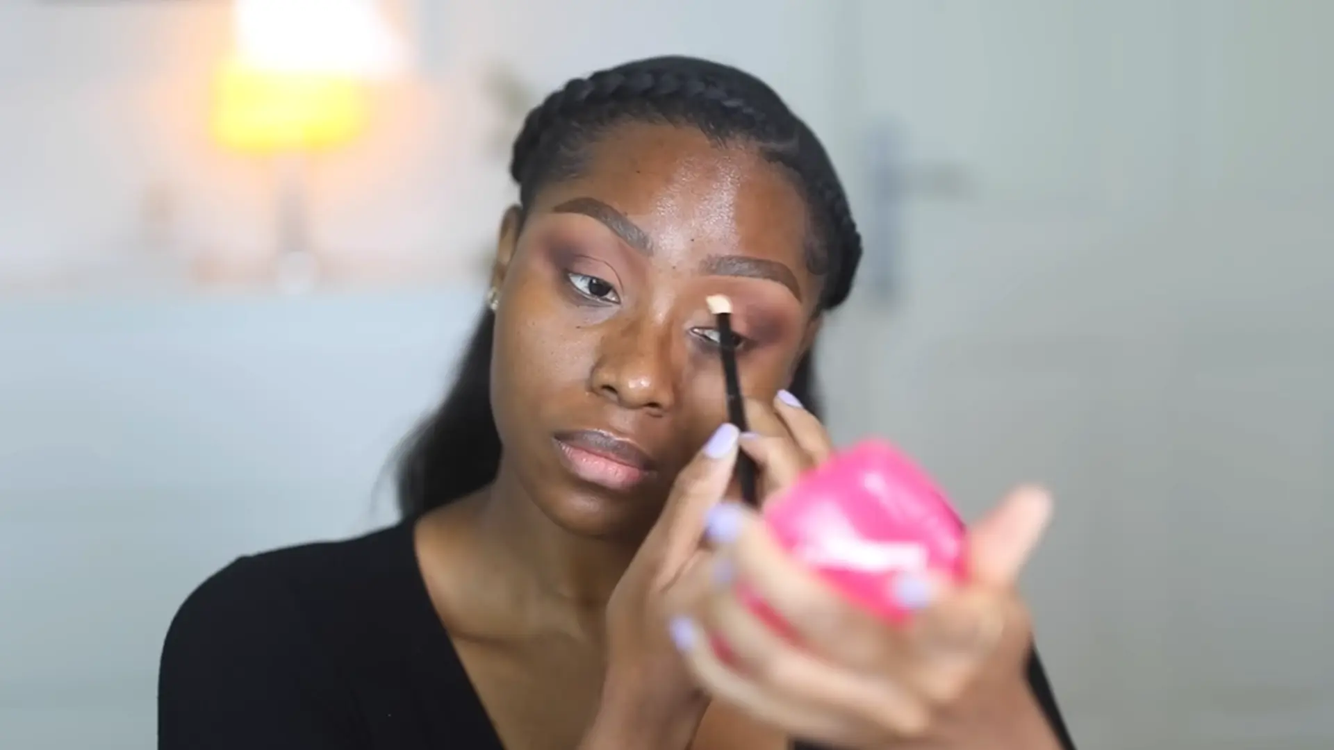 a woman applying eyeshadow with a brush while holding a compact mirror, focused on creating a soft glam eye makeup look with blended warm tones