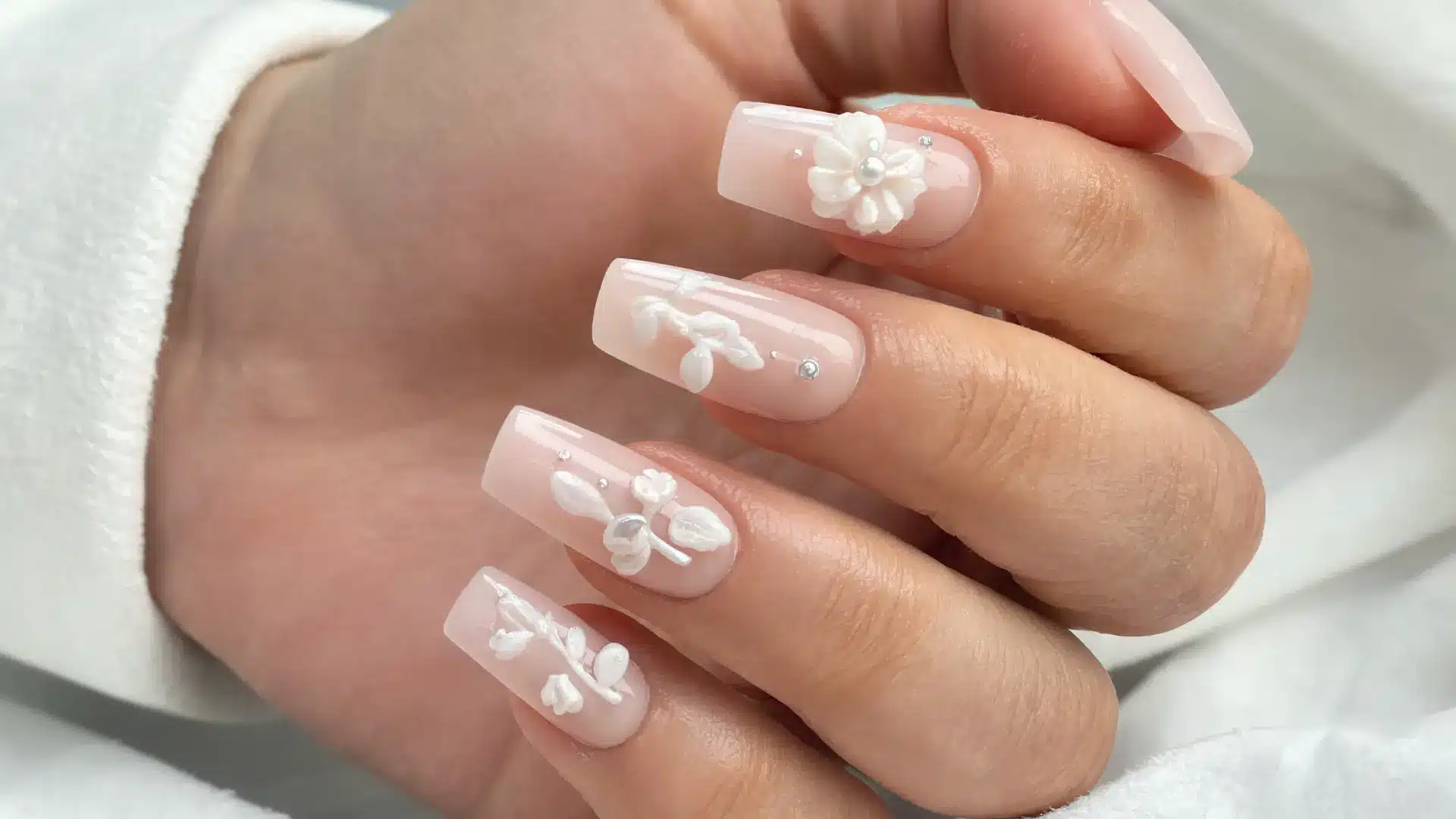 close up minimal 3d nail art coffin nails soft nude base tiny pearls subtle gems delicate floral accents luxury salon light