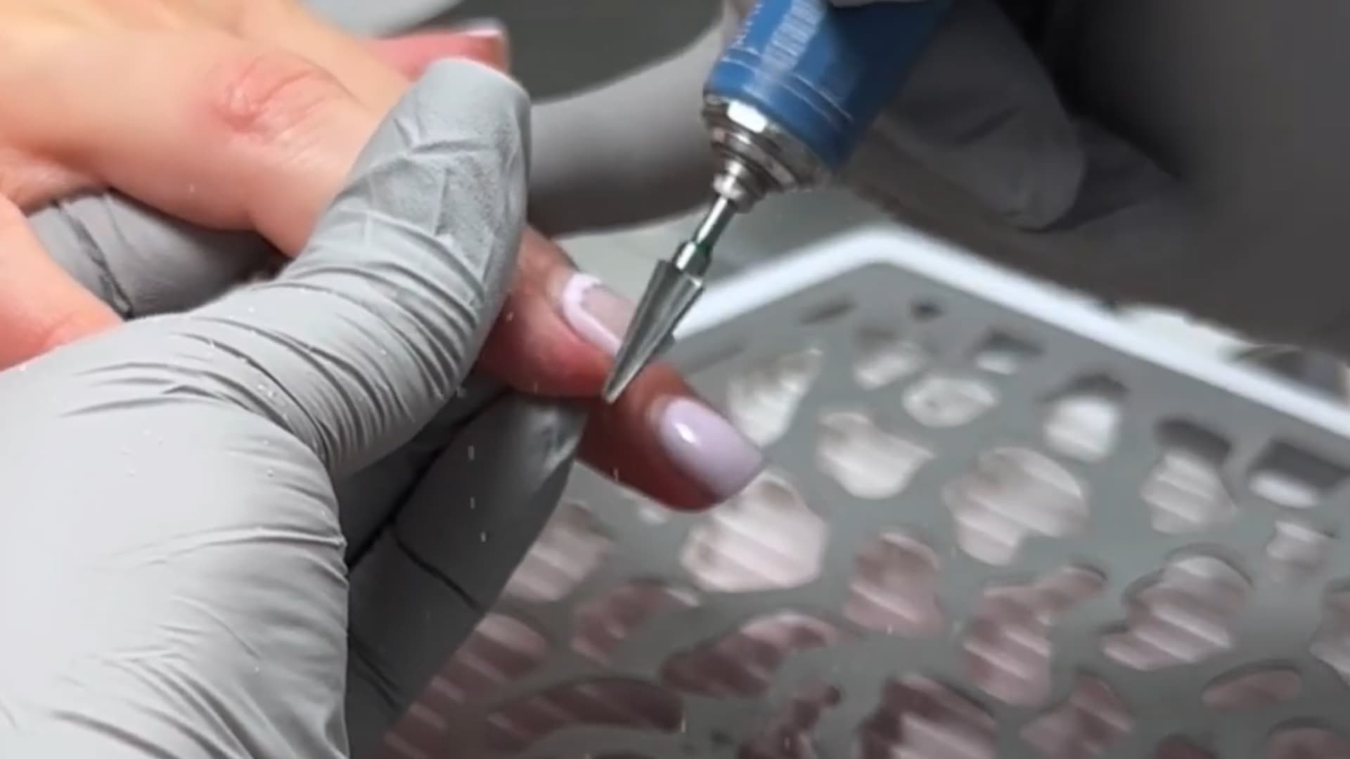 close-up of nail technician using an electric file to remove surface product from natural nails