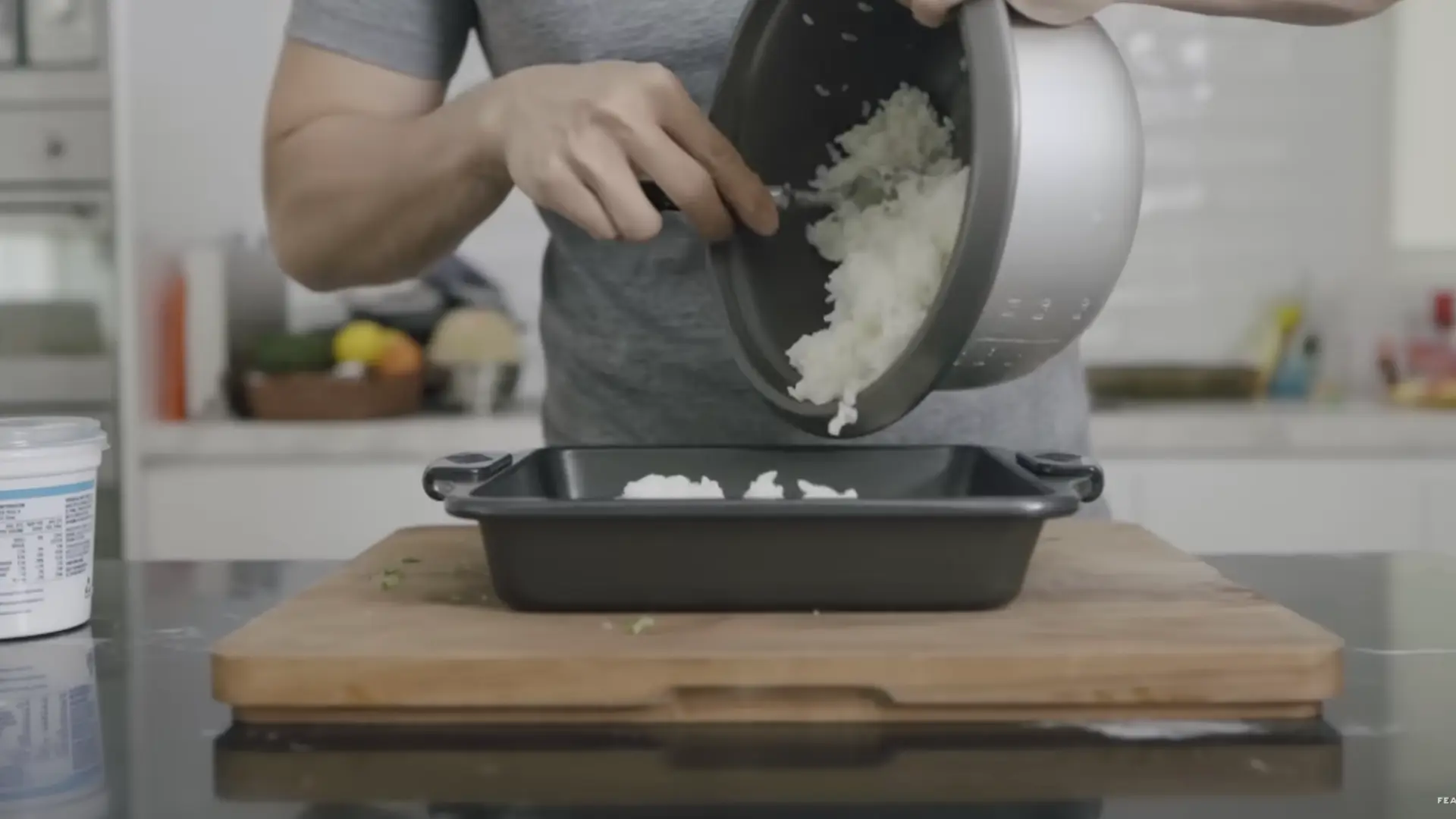 cooked sushi rice being pressed evenly into a baking dish to form a firm base layer .