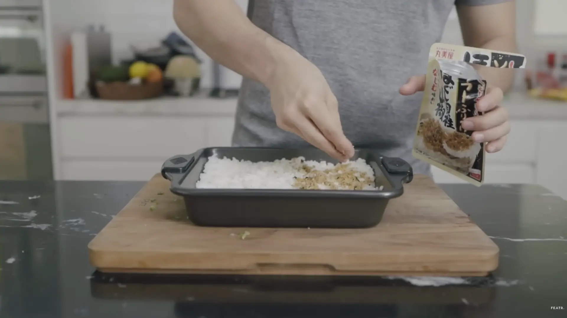 furikake seasoning being sprinkled over pressed sushi rice to add flavor and texture before layering
