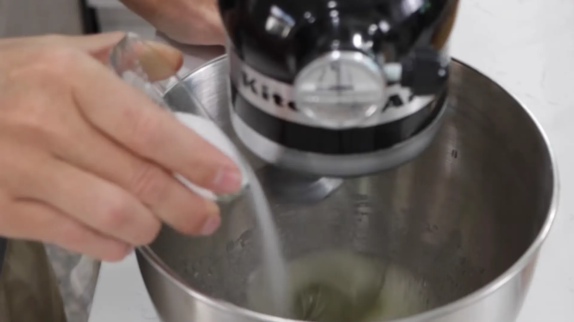 Gradually adding sugar into whipped egg whites while mixing to stabilize foam structure