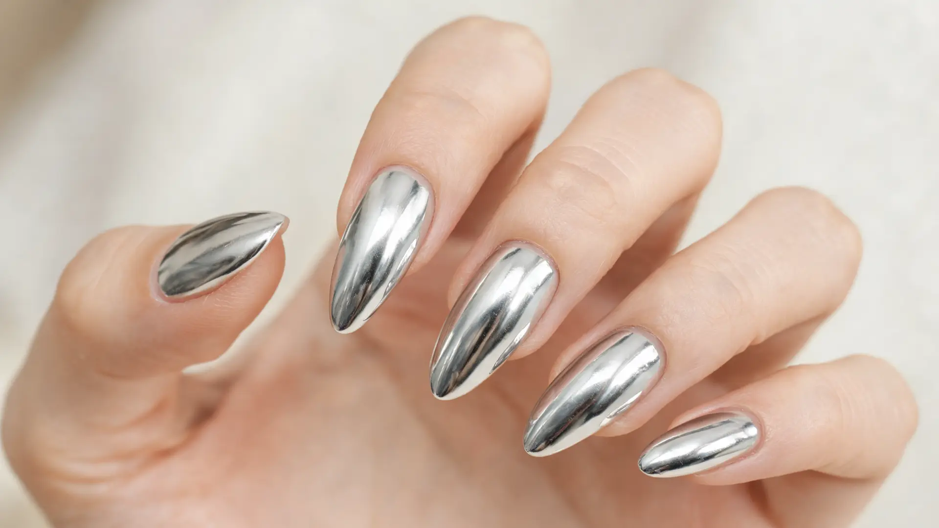 hand with chrome mirror nail enhancements, almond shaped nails, metallic silver reflective finish in soft studio light
