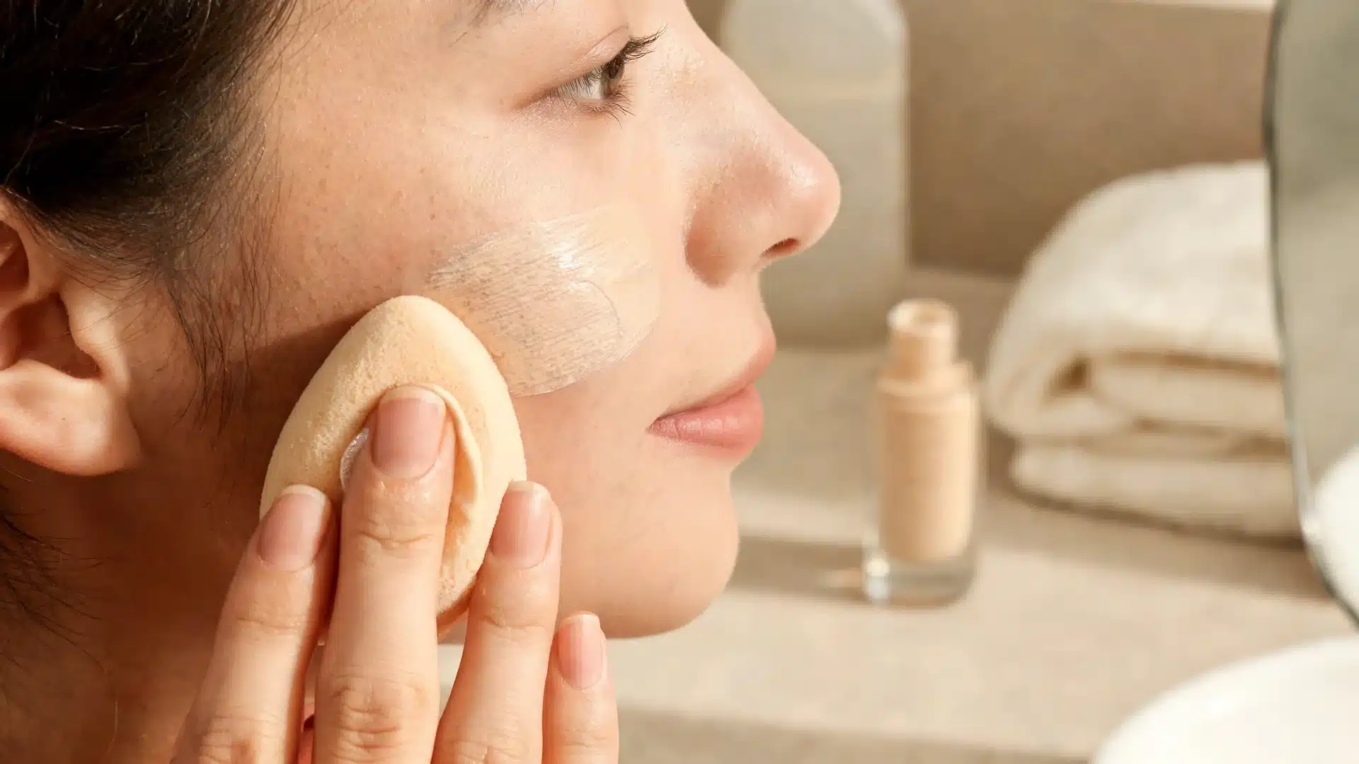 makeup sponge pressing thin foundation layers for a soft skin like finish near the cheek and nose