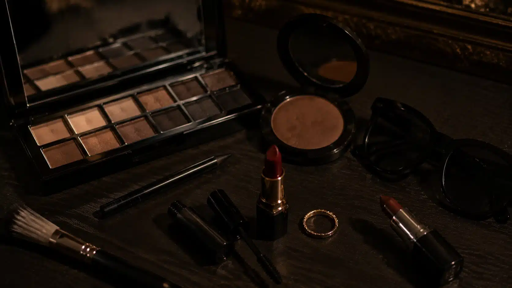 mob wife aesthetic makeup setup with smoky liner, bronzer, and deep red lipstick