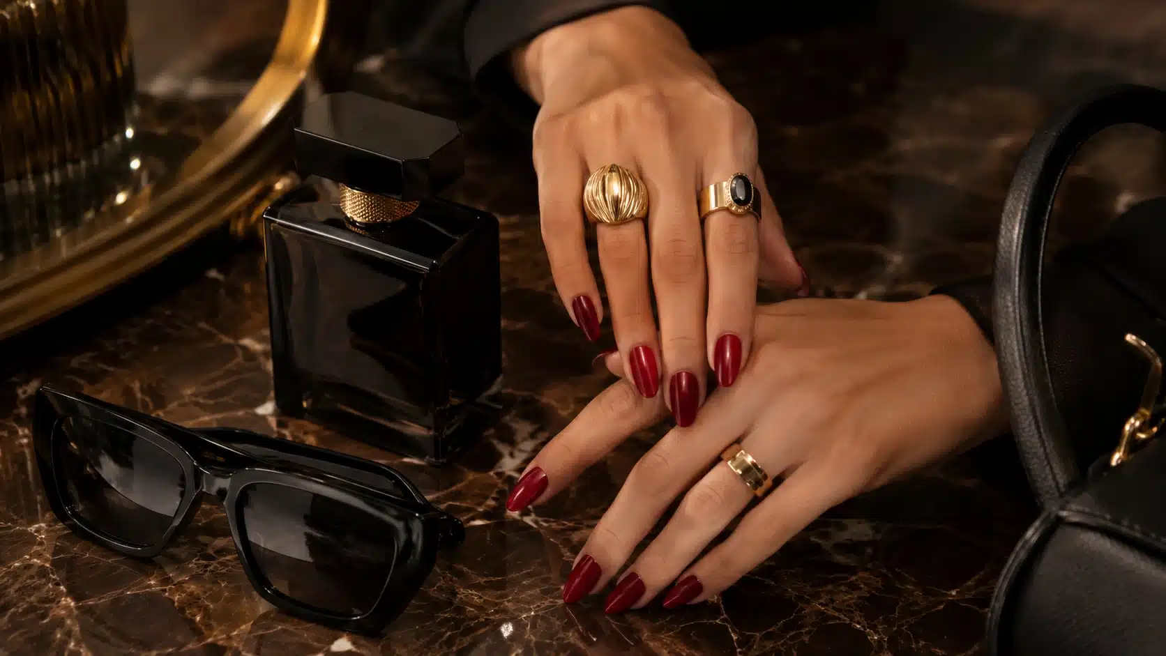 mob wife aesthetic nail details with red polish, gold rings, perfume, and sunglasses