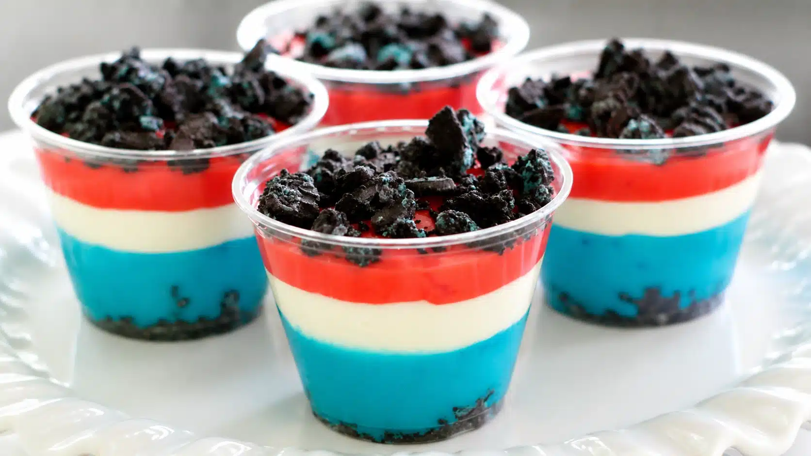 Red, white, and blue layered dessert cups topped with crushed cookies, arranged on a white tray (2)