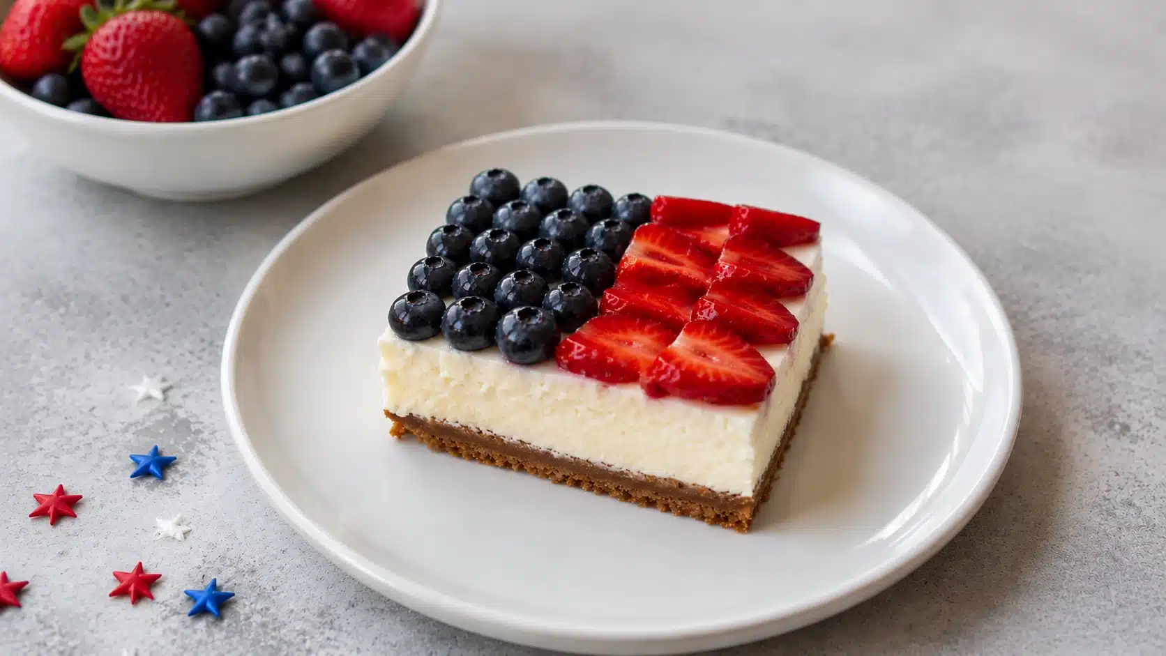 Slice of strawberry cheesecake on a plate topped with fresh strawberries and blueberries, with a bowl of berries in the background