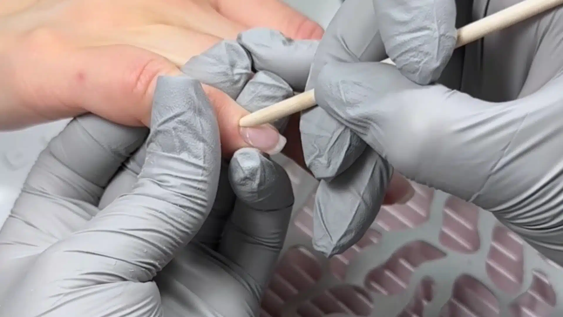 technician using a wooden stick to gently push back cuticles on natural nails with gloves