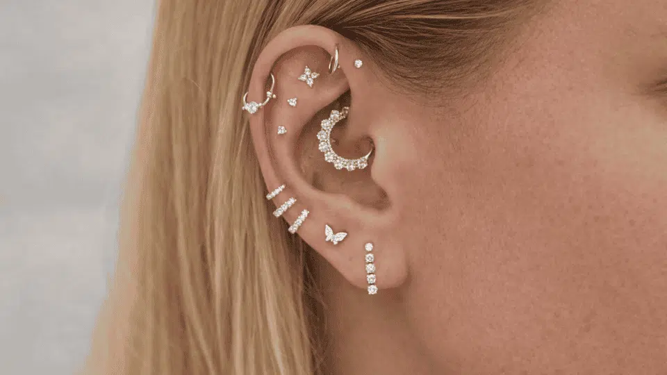 side view of blonde woman with full ear piercings, silver hoops and studs, soft light and neutral backdrop