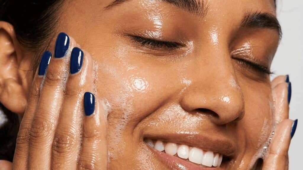 woman with glossy oily skin washing face with foaming cleanser, blue nail polish, close up skincare routine
