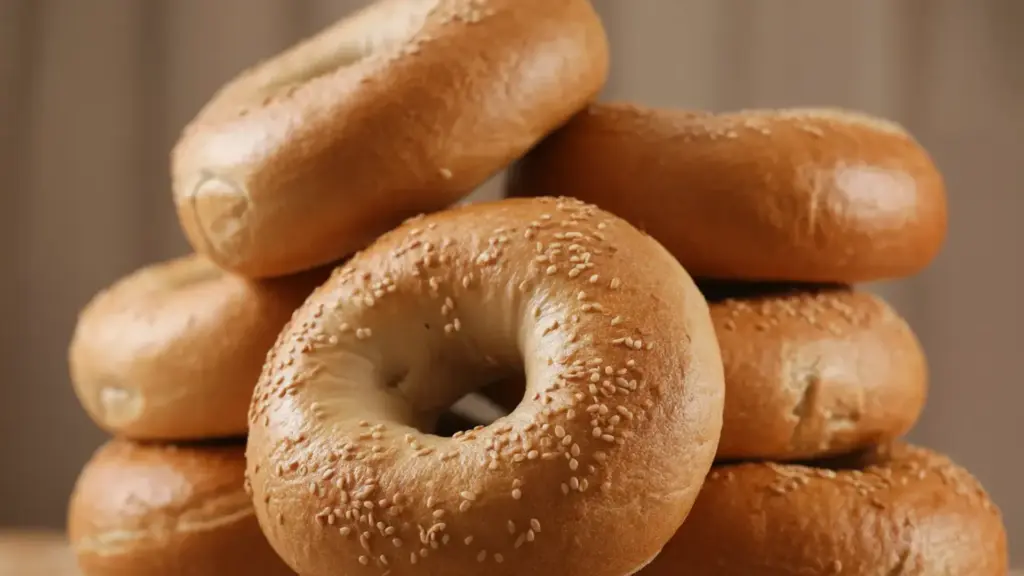 a stack of golden brown toasted sesame seed bagels piled on top of each other against a soft brown background