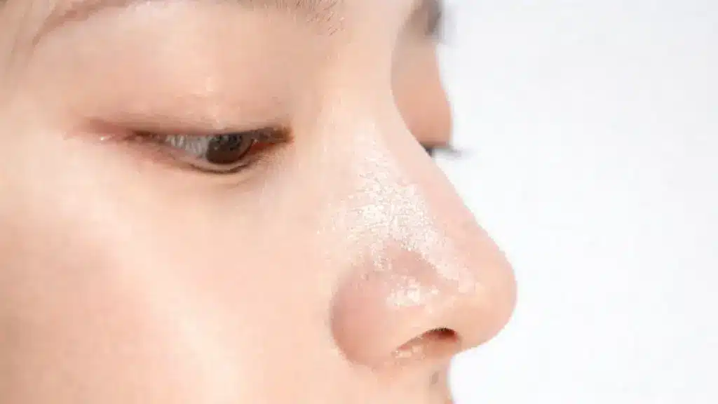 close up of nose showing visible oily shine and skin texture with pores reflecting light in natural skincare lighting